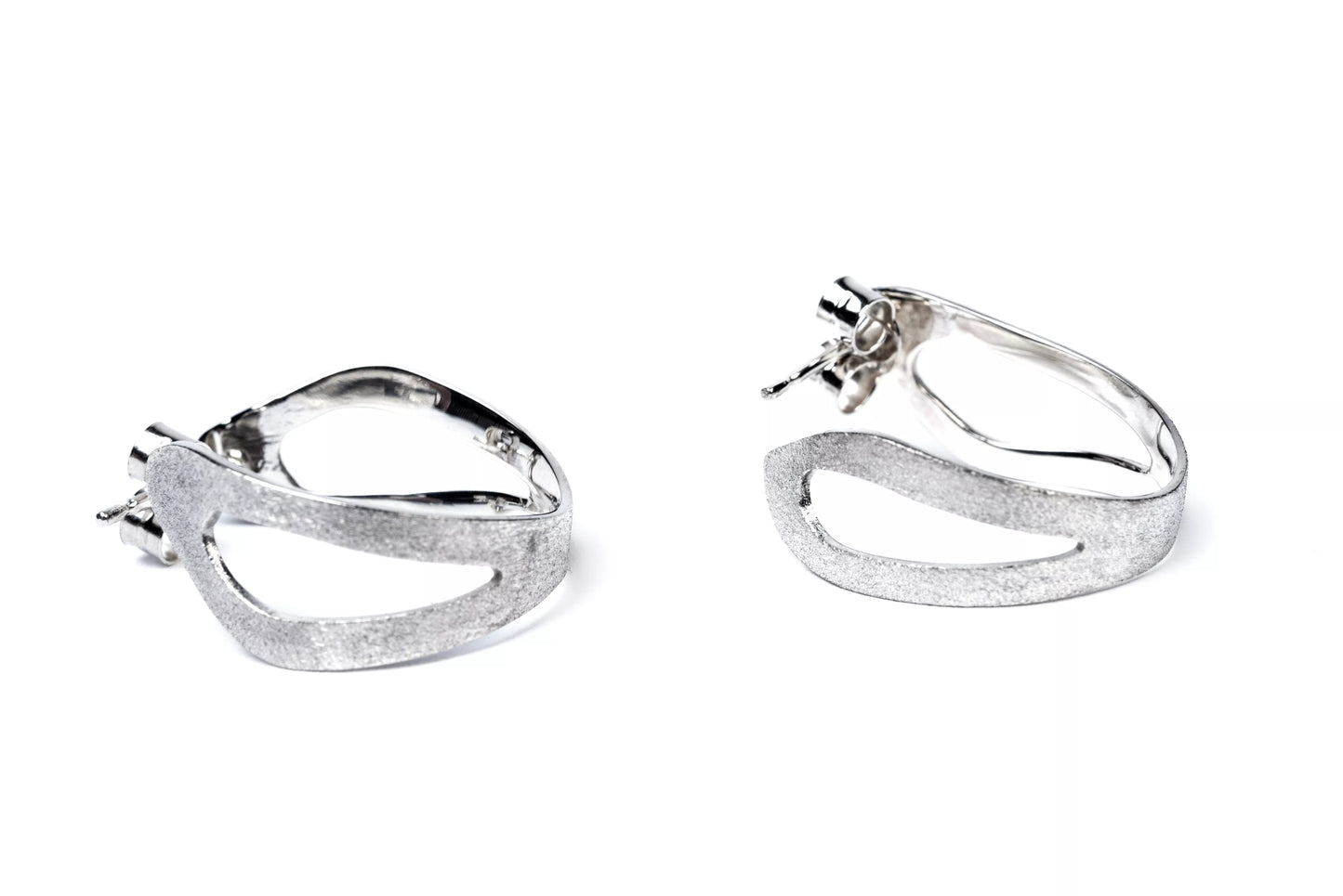 Pair of sterling silver sculptural hoop earrings with cut out sections on a white background