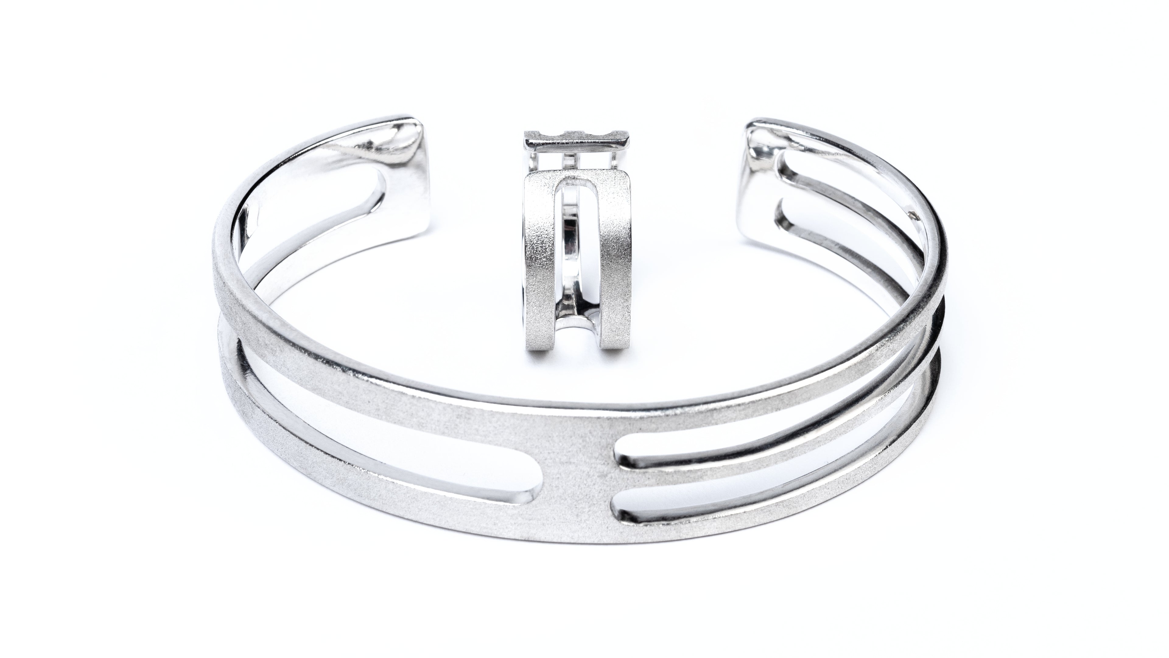 A silver mens ring and a silver mens cuff. They have a similar geometric linear design with cut out sections. They have a frosted external finish and shiny internal finish.