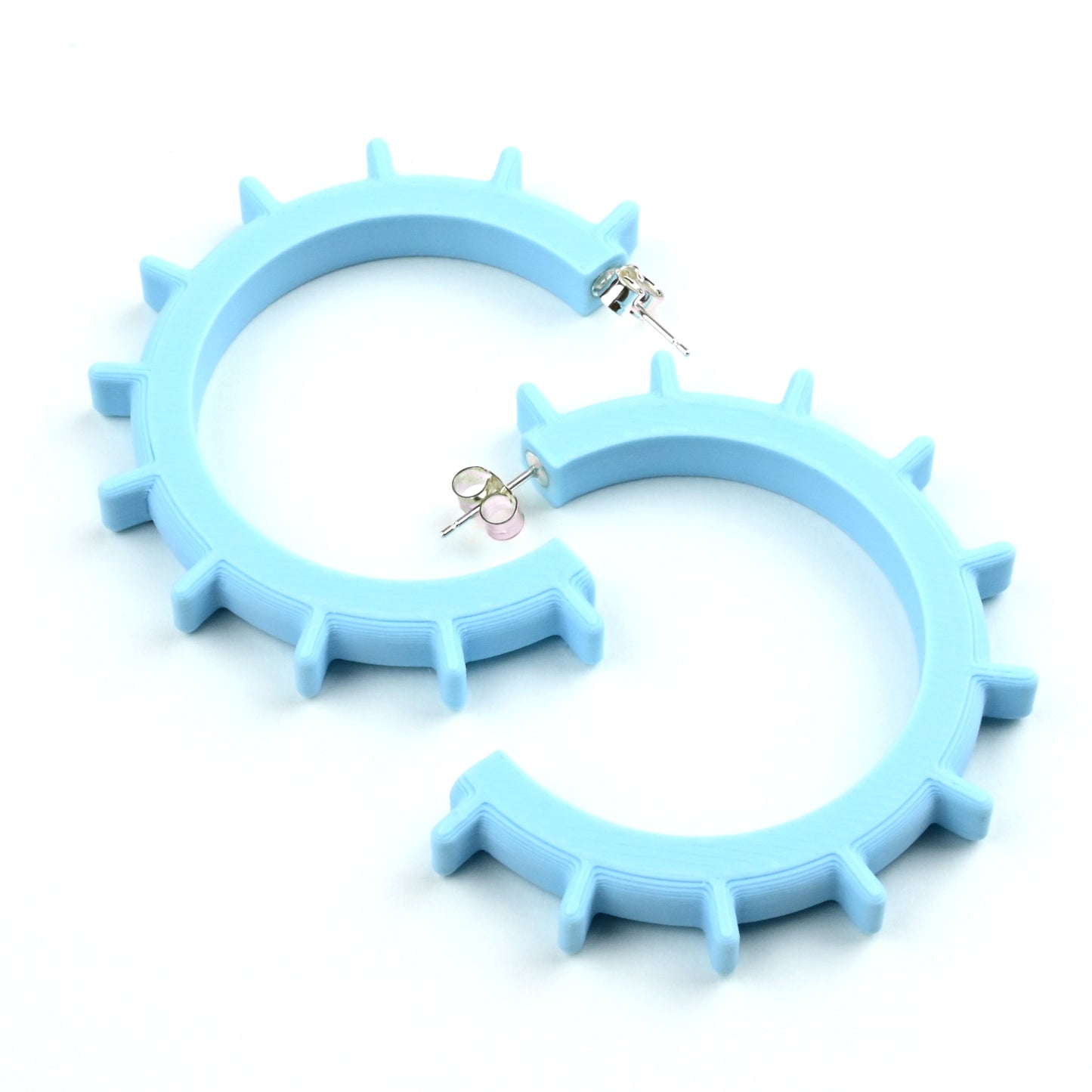 Pair of large pale blue cog shaped hoop earings with silver ear posts on a white background