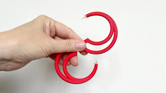 Pair of Roxwoods statement red hoop earrings held in a womens hand