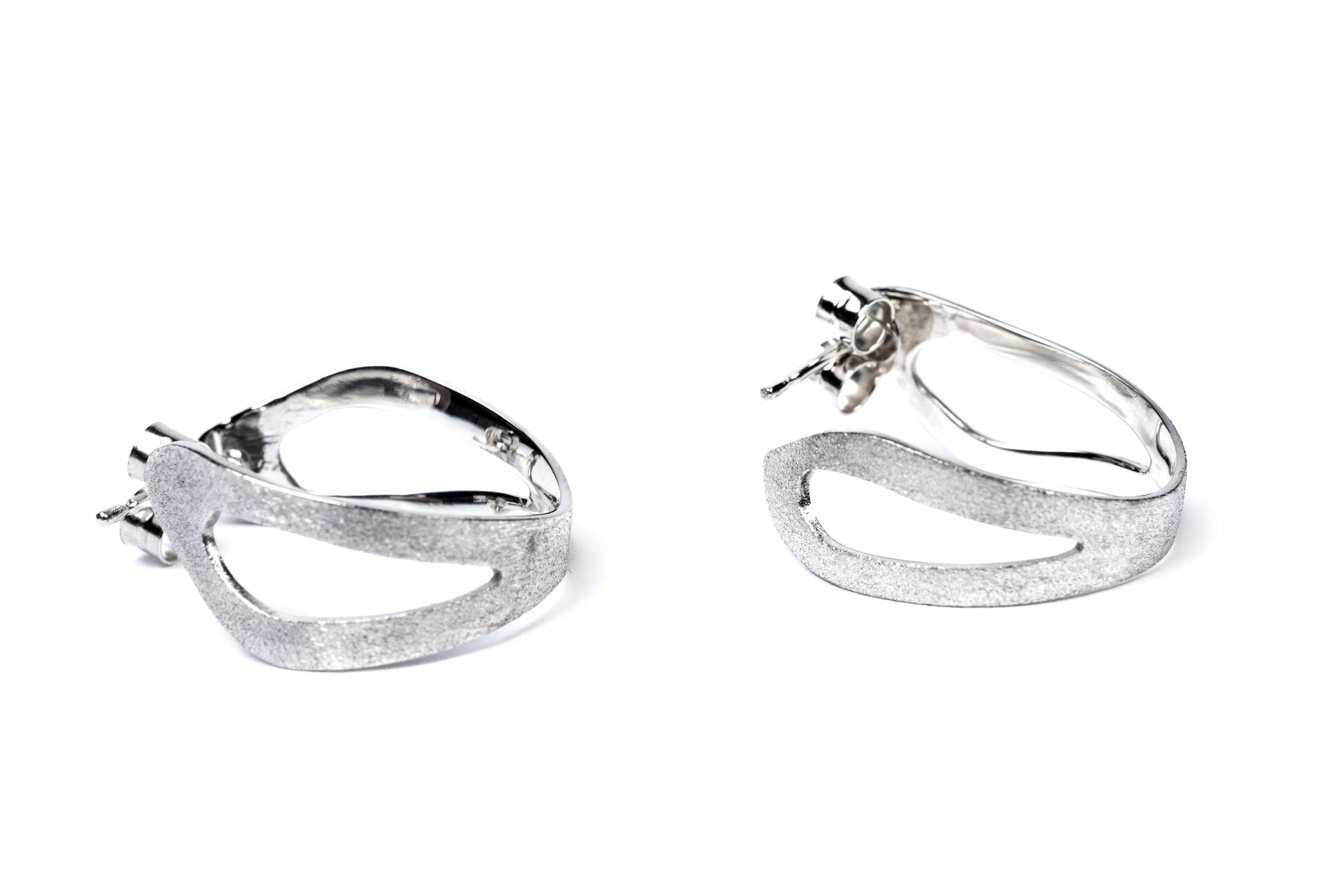Pair of sterling silver sculptural hoop earrings with cut out sections on a white background