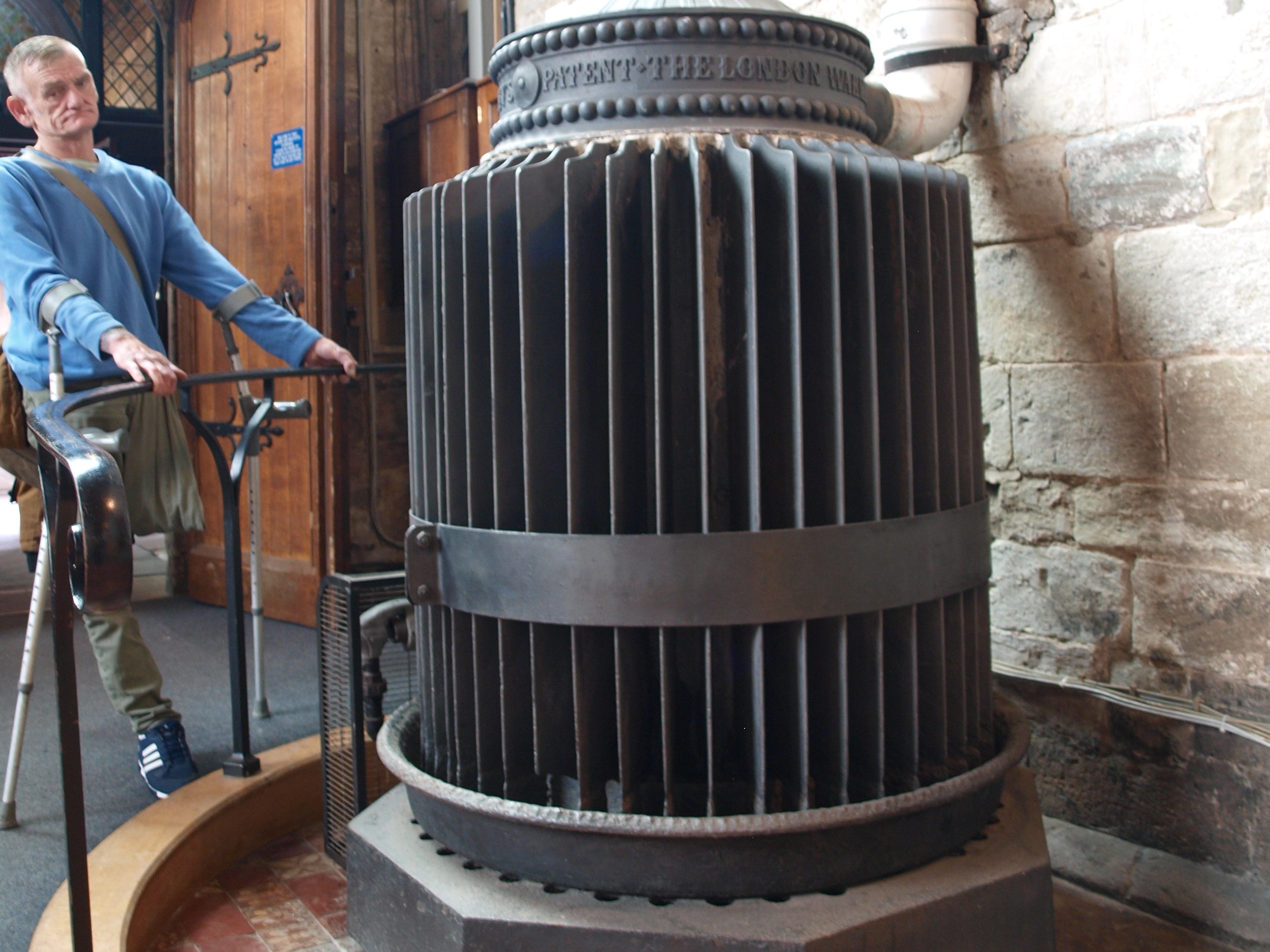 Black iron radiator with round form and many fins sticking out from a central core.  There is writing on the top of the radiator which reads 'patent the London'