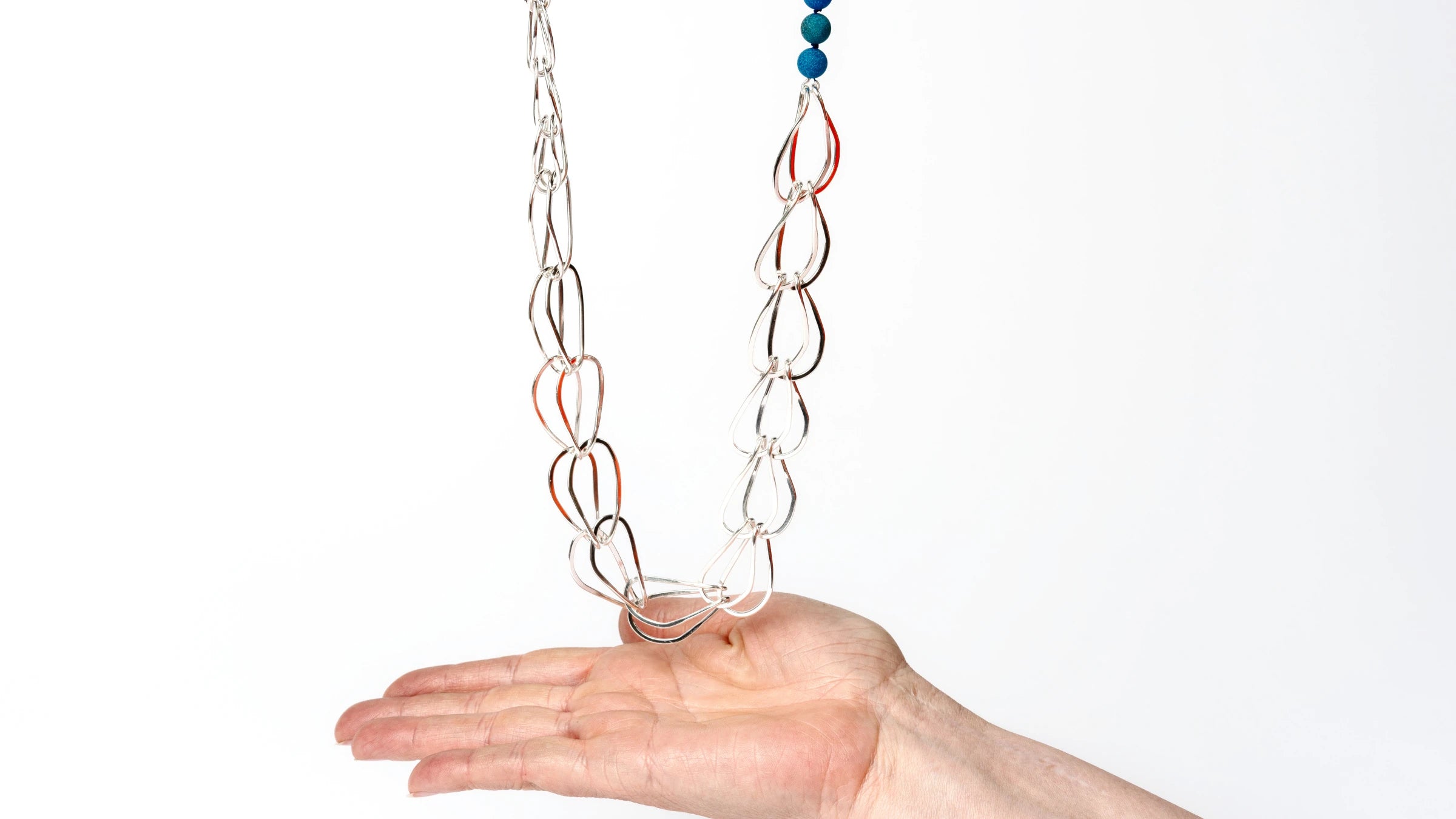 Hand below a large silver chain with blue gemstone beads against a white background