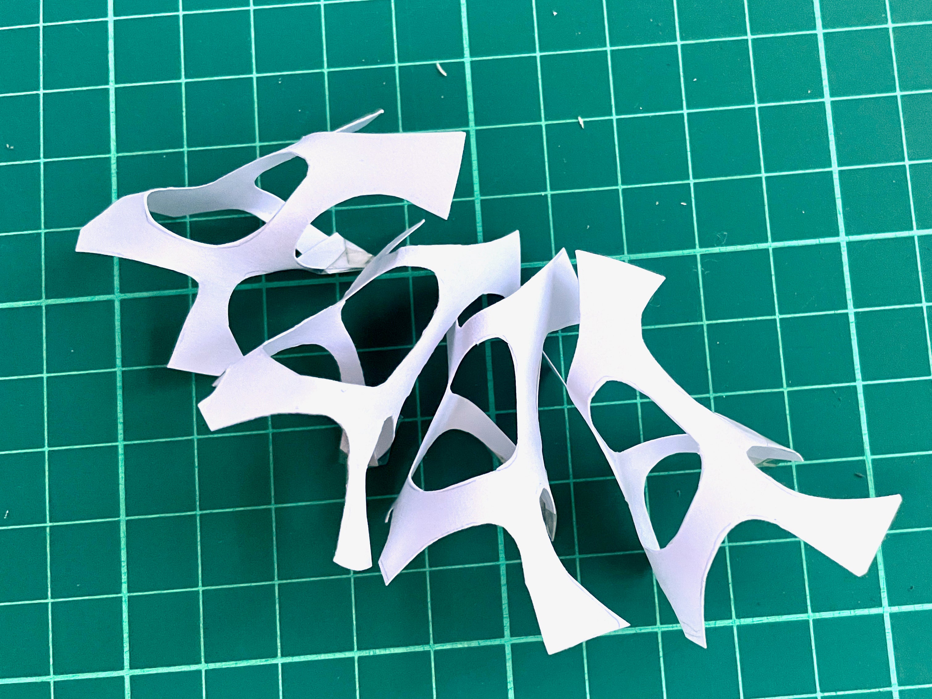 White paper abstract shapes curved and repeated to form a pattern.  The background is a green cutting mat.