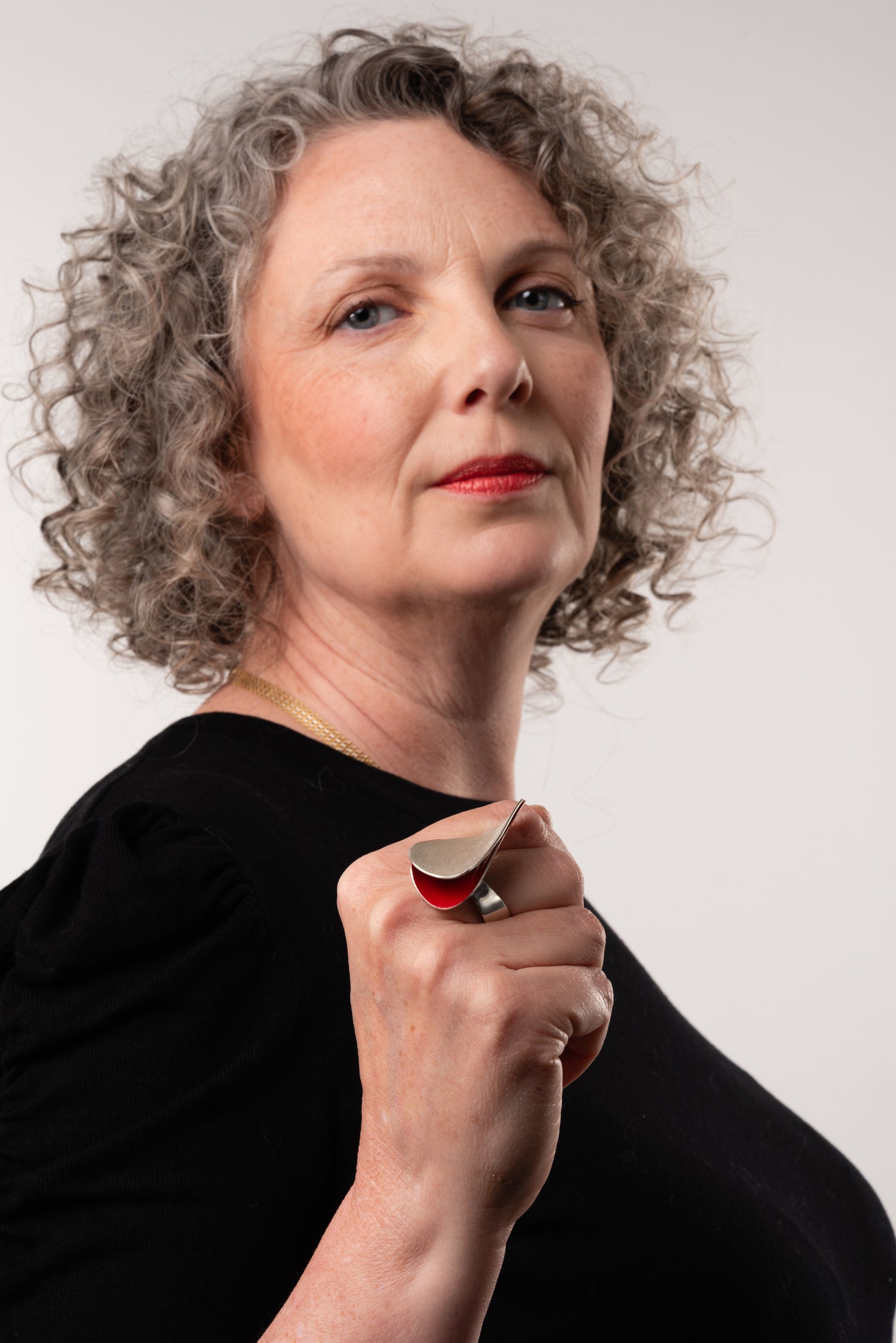 A woman with curly hair in a black dress wearing a large contemporary silver and red ring with a sculptural shape.