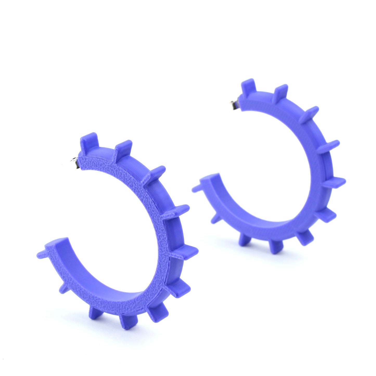 Pair of large purple cog shaped hoop earings with silver ear posts on a white background