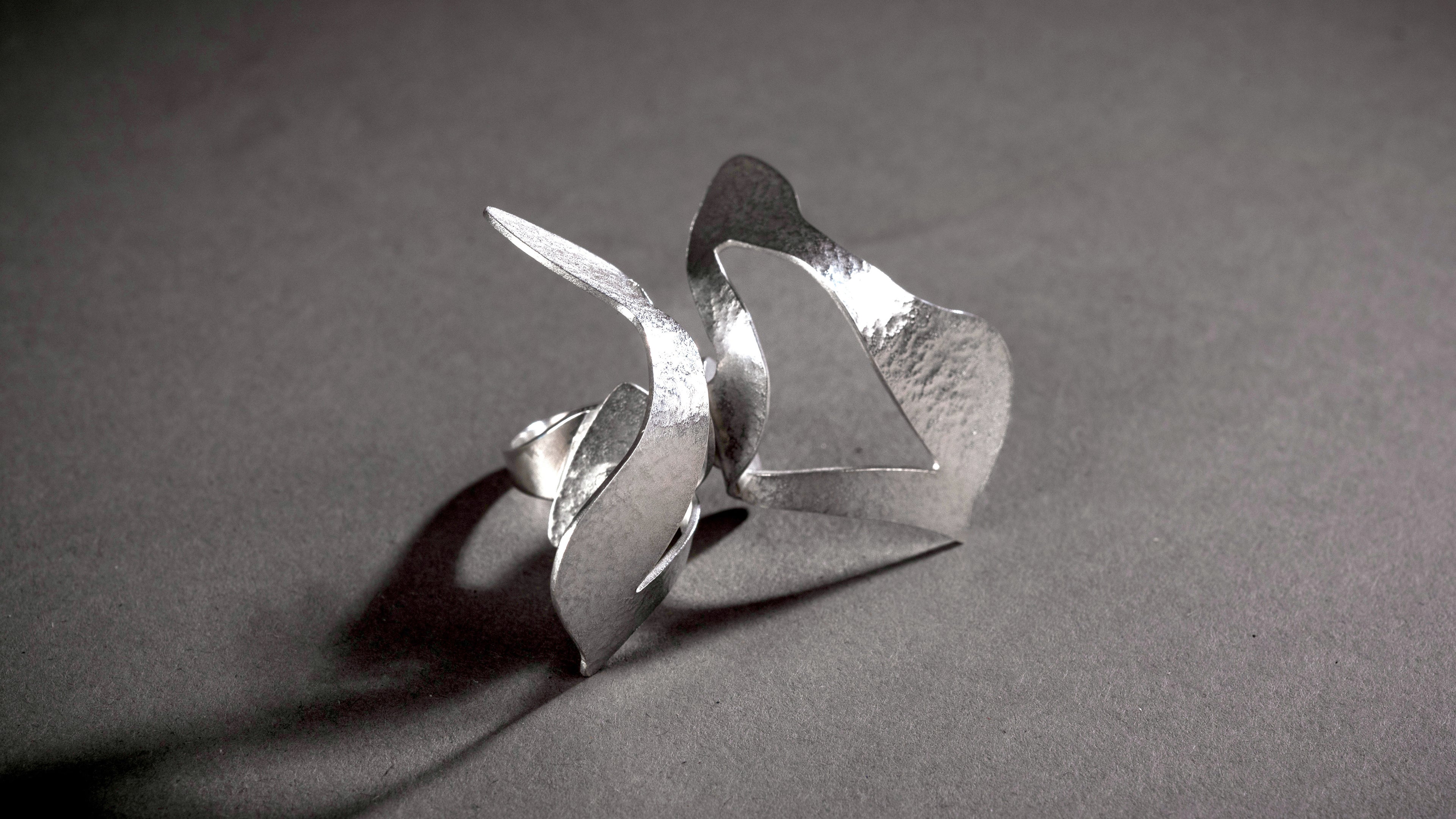 Big silver cocktail ring made with an abstract butterfly shape set on top of a simple silver ring band.  The silver has a textured surface and shiny burnished edges.