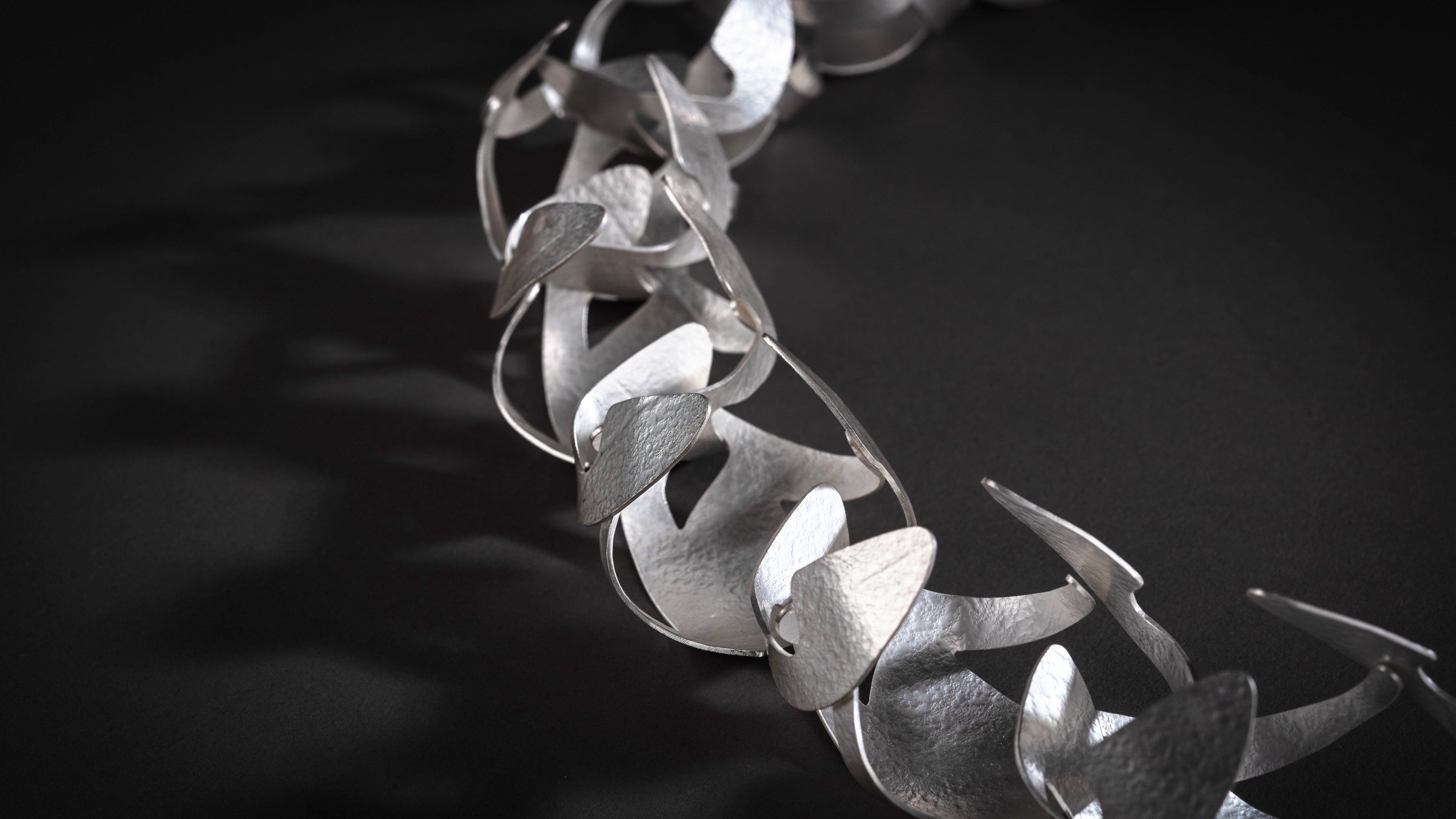 Large silver choker style necklace made up of three dimensional forms linked together.  Each form has a textured surface and shiny edges.  