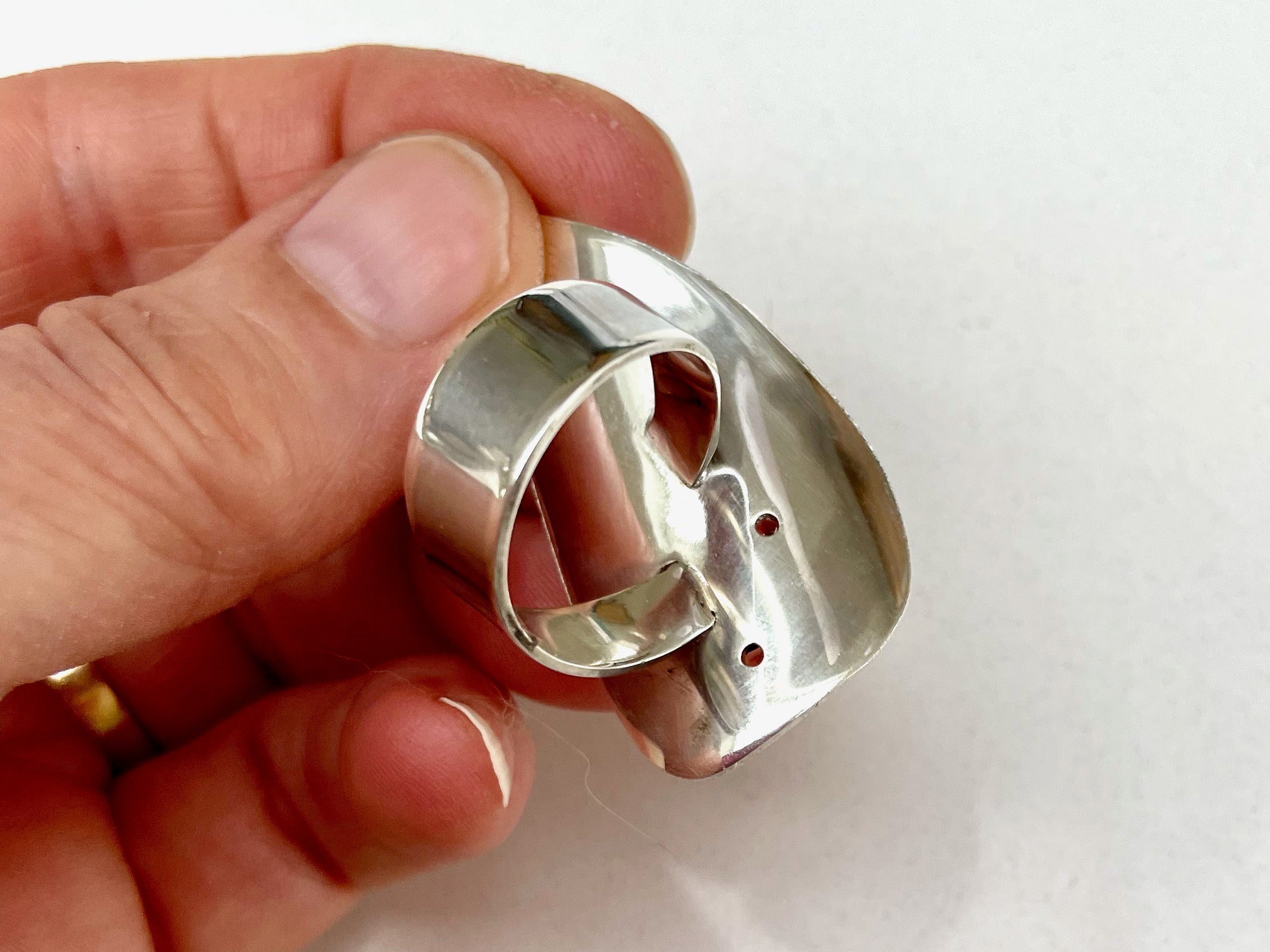 The back of a silver ring showing a ring band with a twist.  The ring is polished and very shiny.  It is being held in a hand.