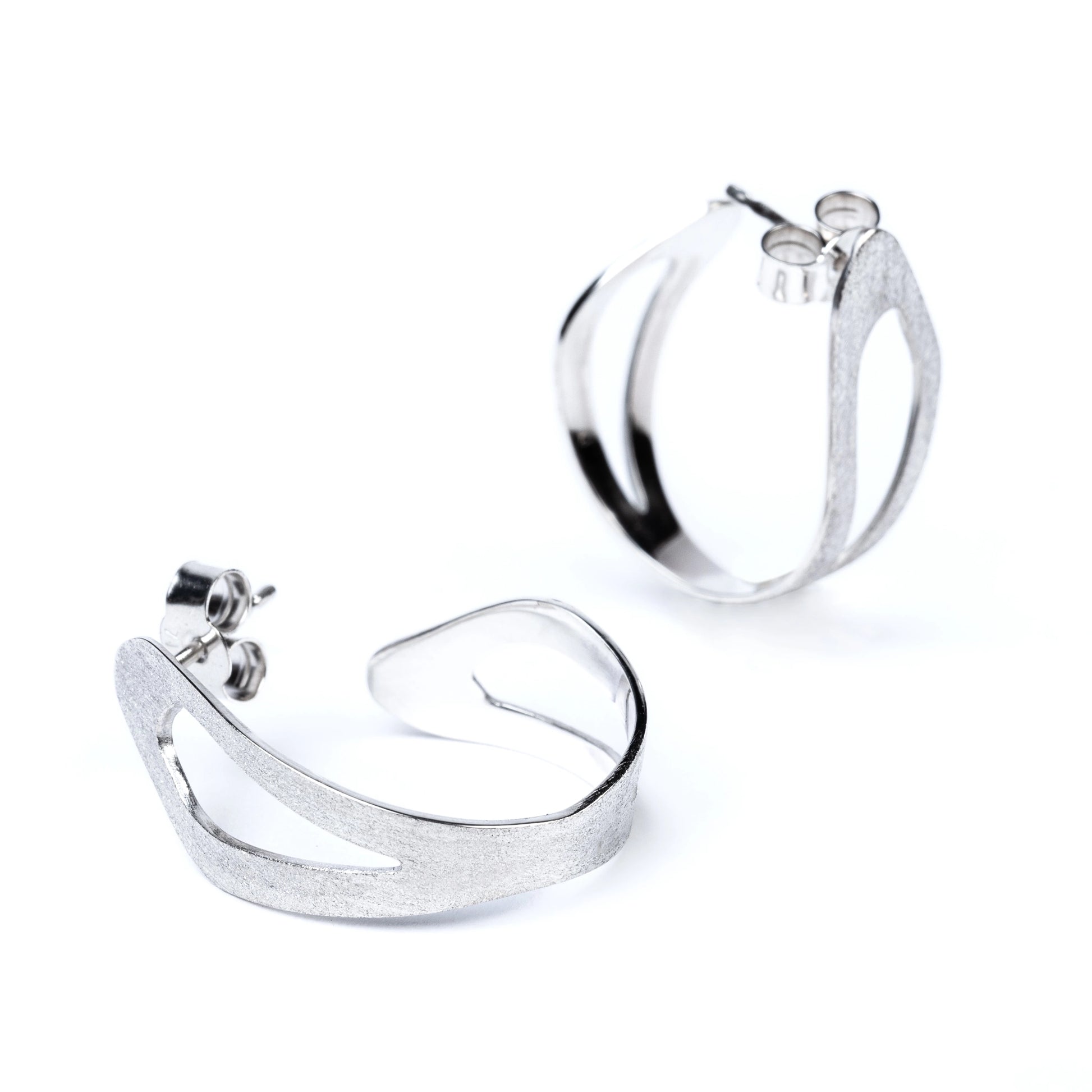 Pair of organic shaped silver hoop earrings with cut out areas on a white background