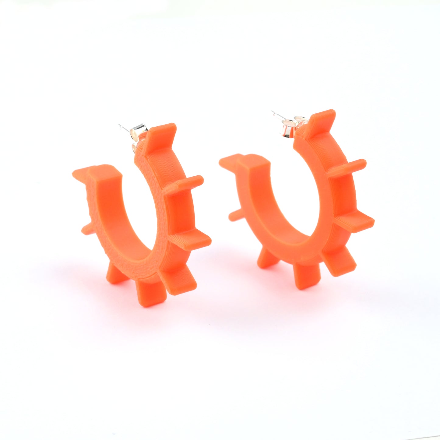 Orange hoop earrings with ridged design and silver ear posts on a white background