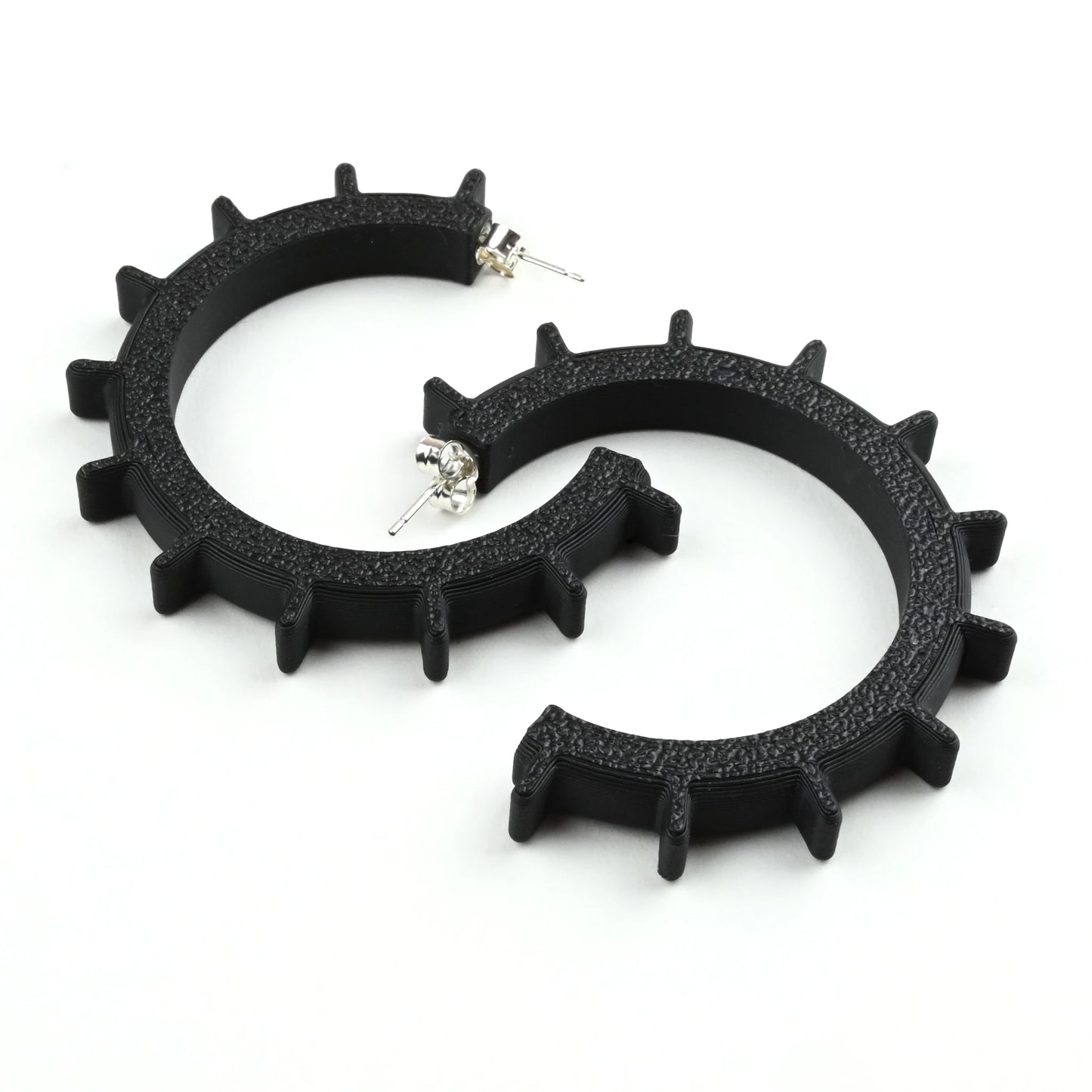 Medium sized black gear shaped hoop earrings with a textured surface on a white background