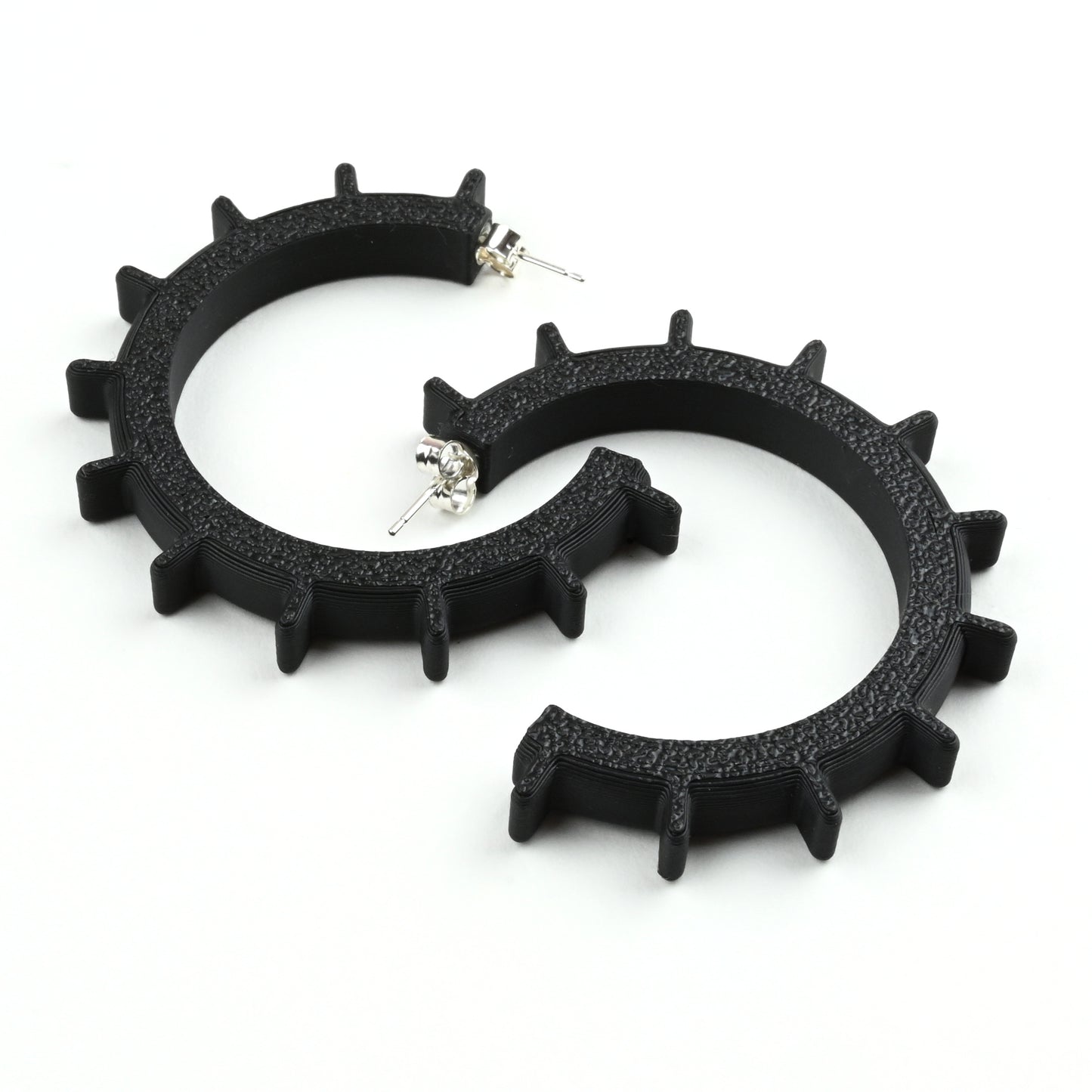 Black gear shaped hoop earrings with silver posts on a white background