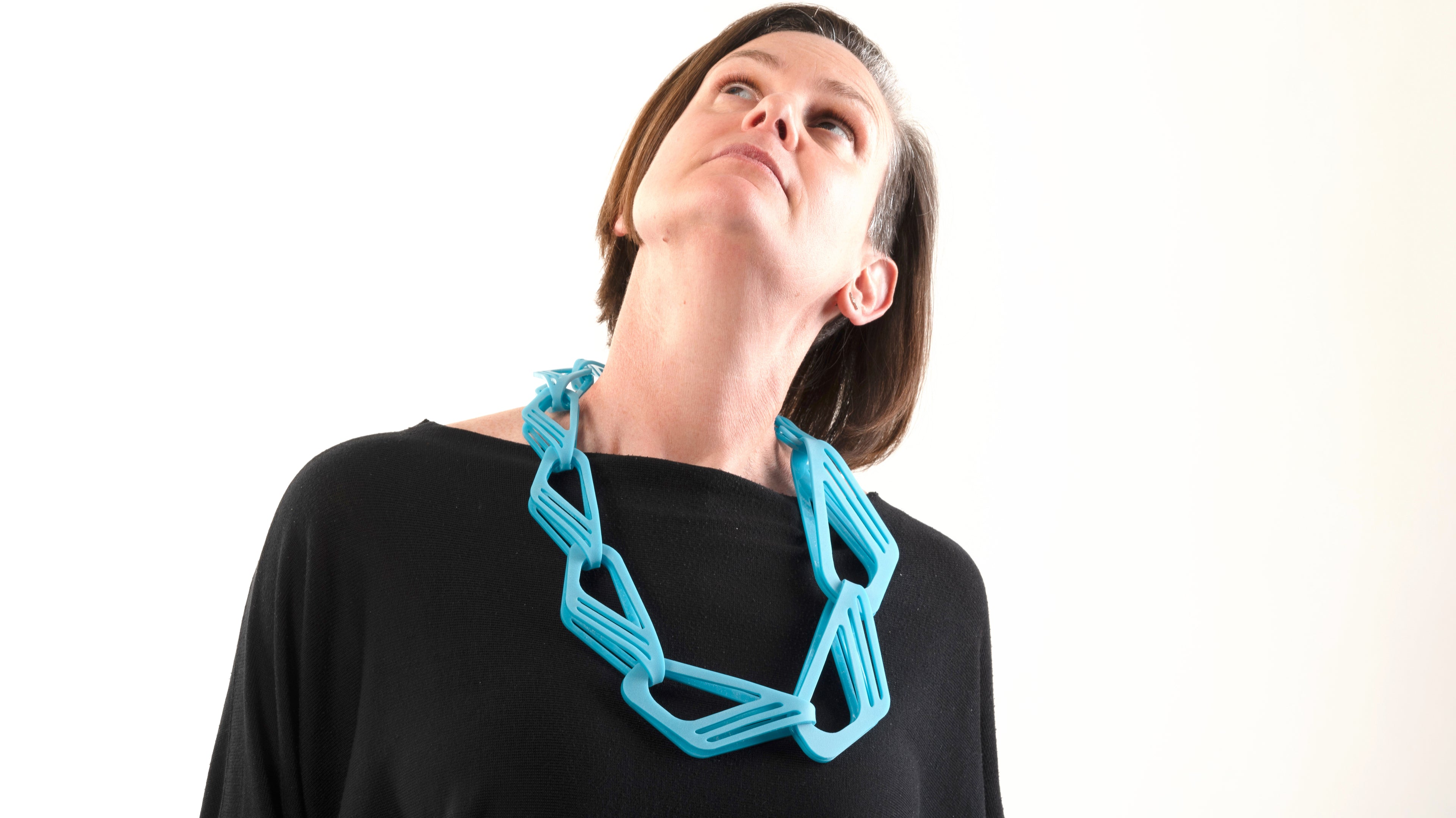 Large blue acrylic chain worn by a women.  She is wearing a black top and looking upwards.