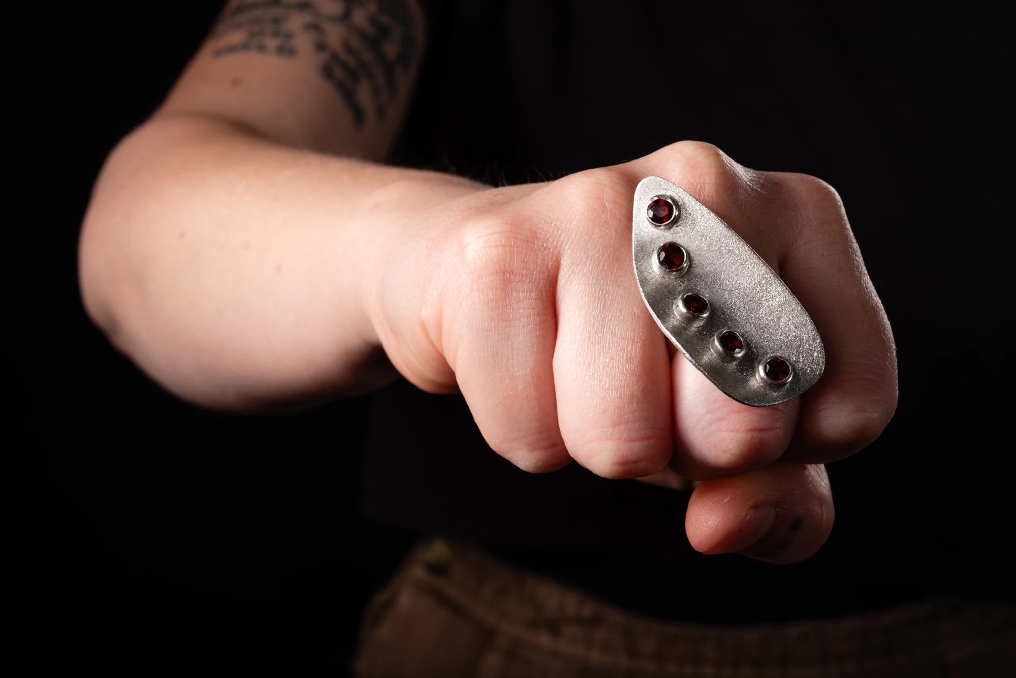 Hand wearing a silver ring with embedded red garnet stones against a dark background