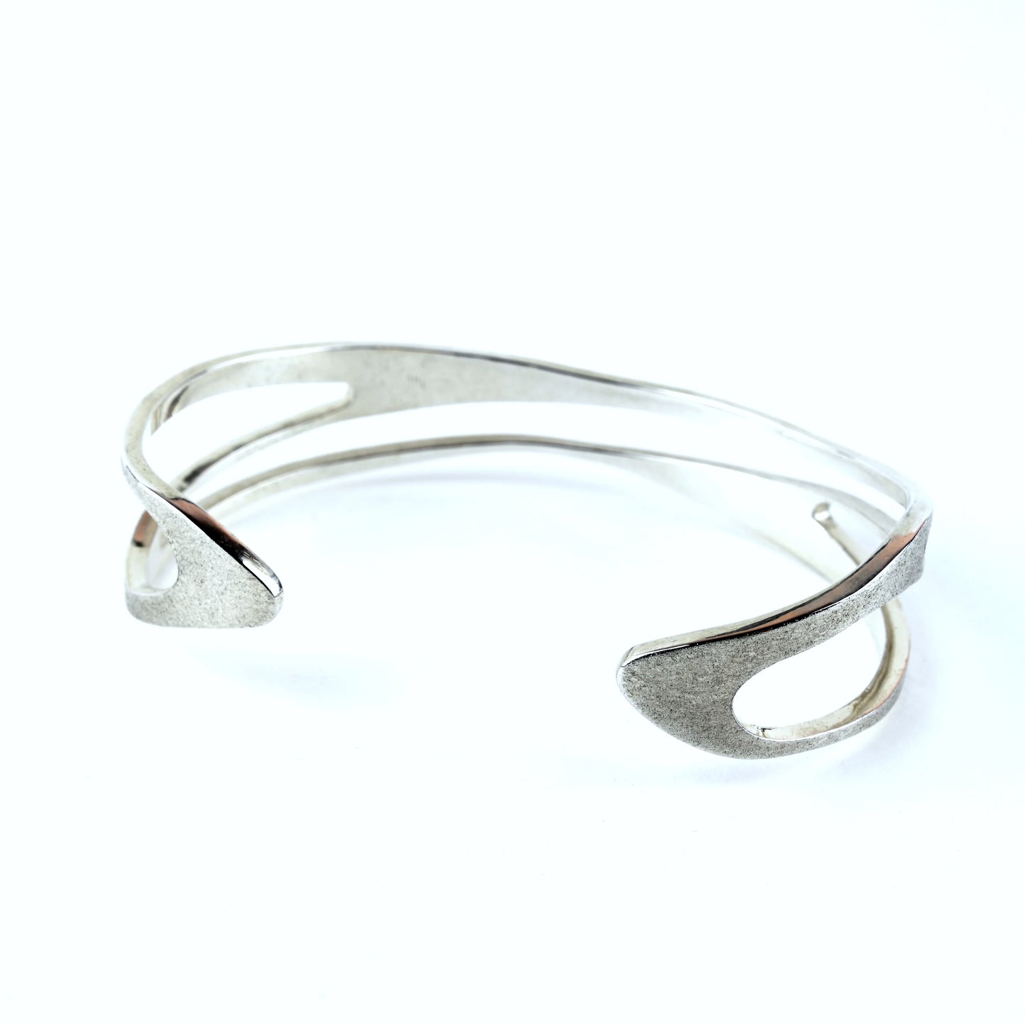 Silver cuff bracelet with curved shape and curved cut out areas on a white background