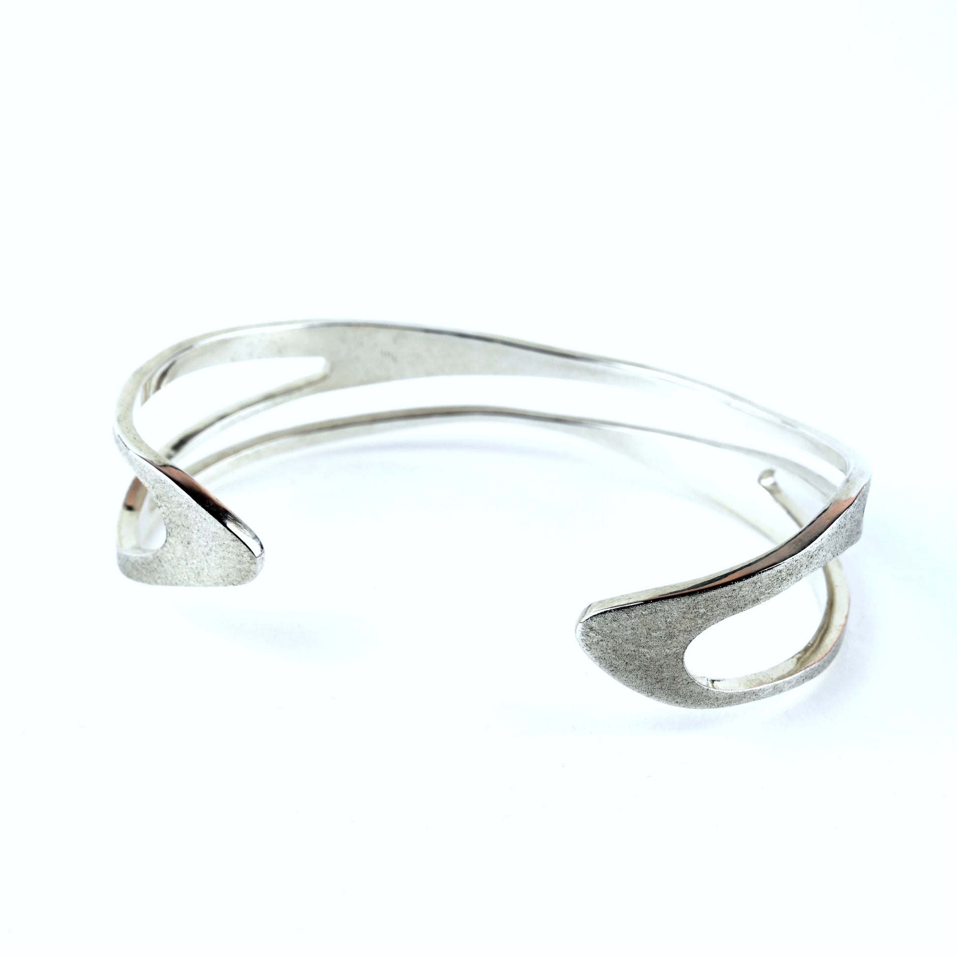 Silver cuff bracelet with curved shape and curved cut out areas on a white background