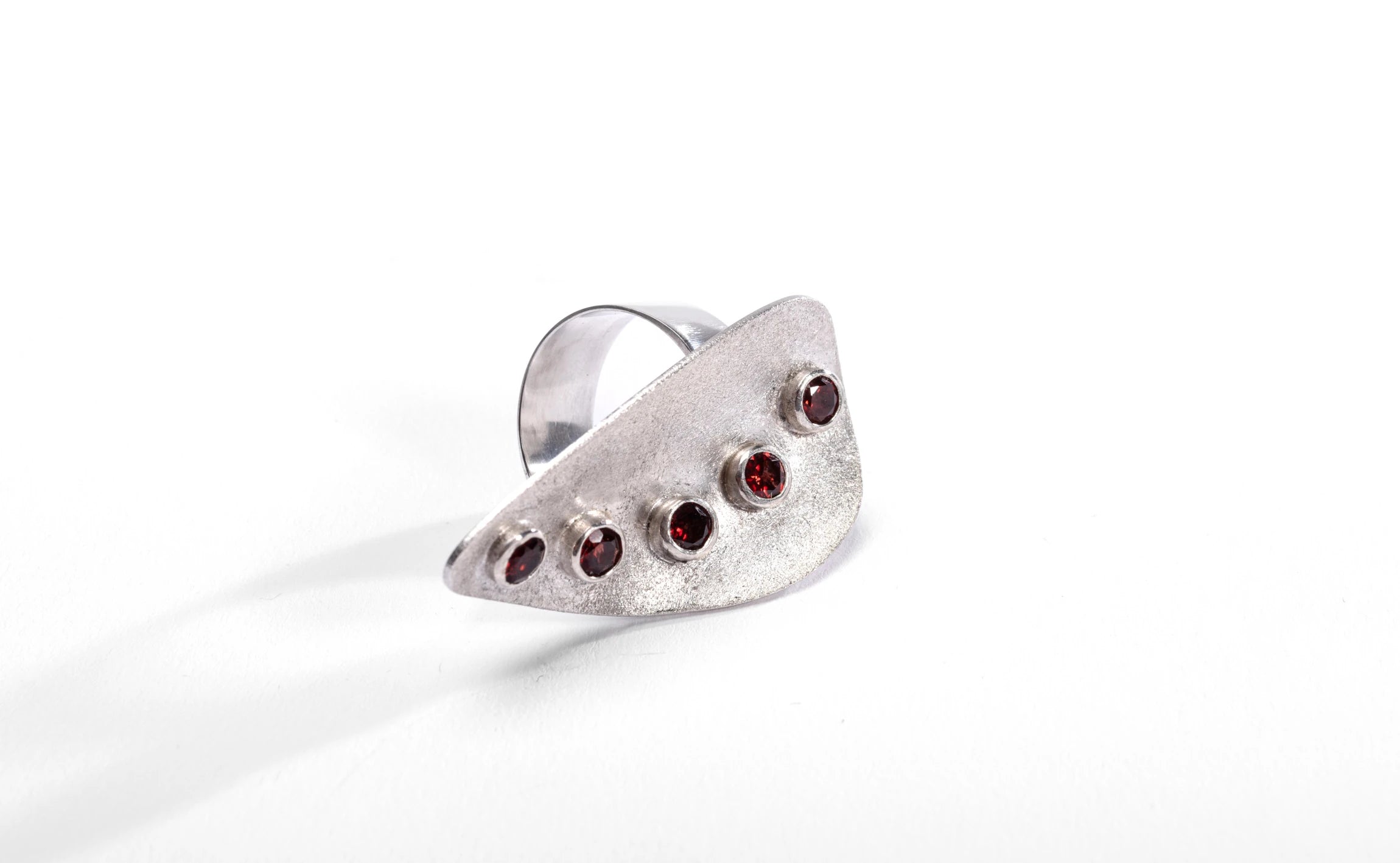 Silver statement ringwith frosted exterior finish and bezel set red garnet gemstones on a white background