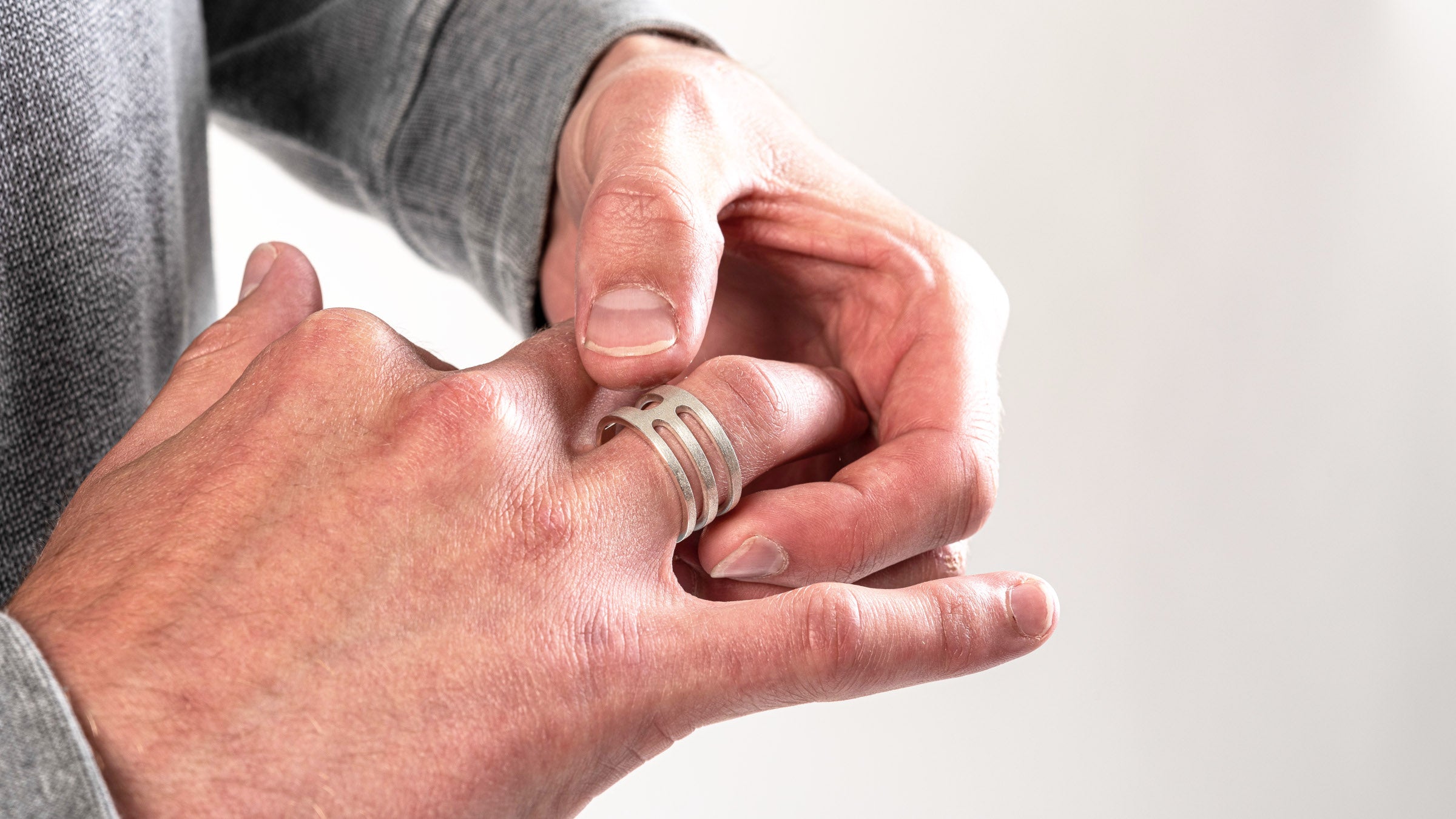 A mans hand wearing a silver ring with a geometric cut out design
