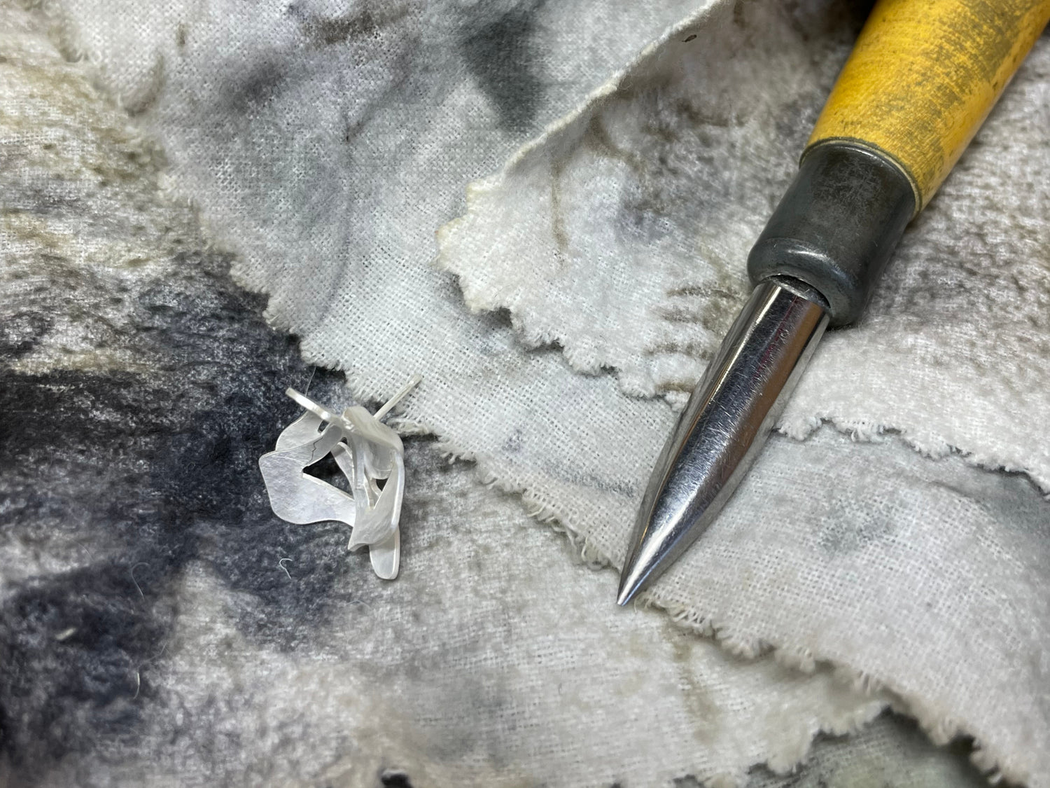 Contemporary sterling silver ear stud with fluid organic shape being polished, next to a metal burnisher used to bright finish the edges of the earring.