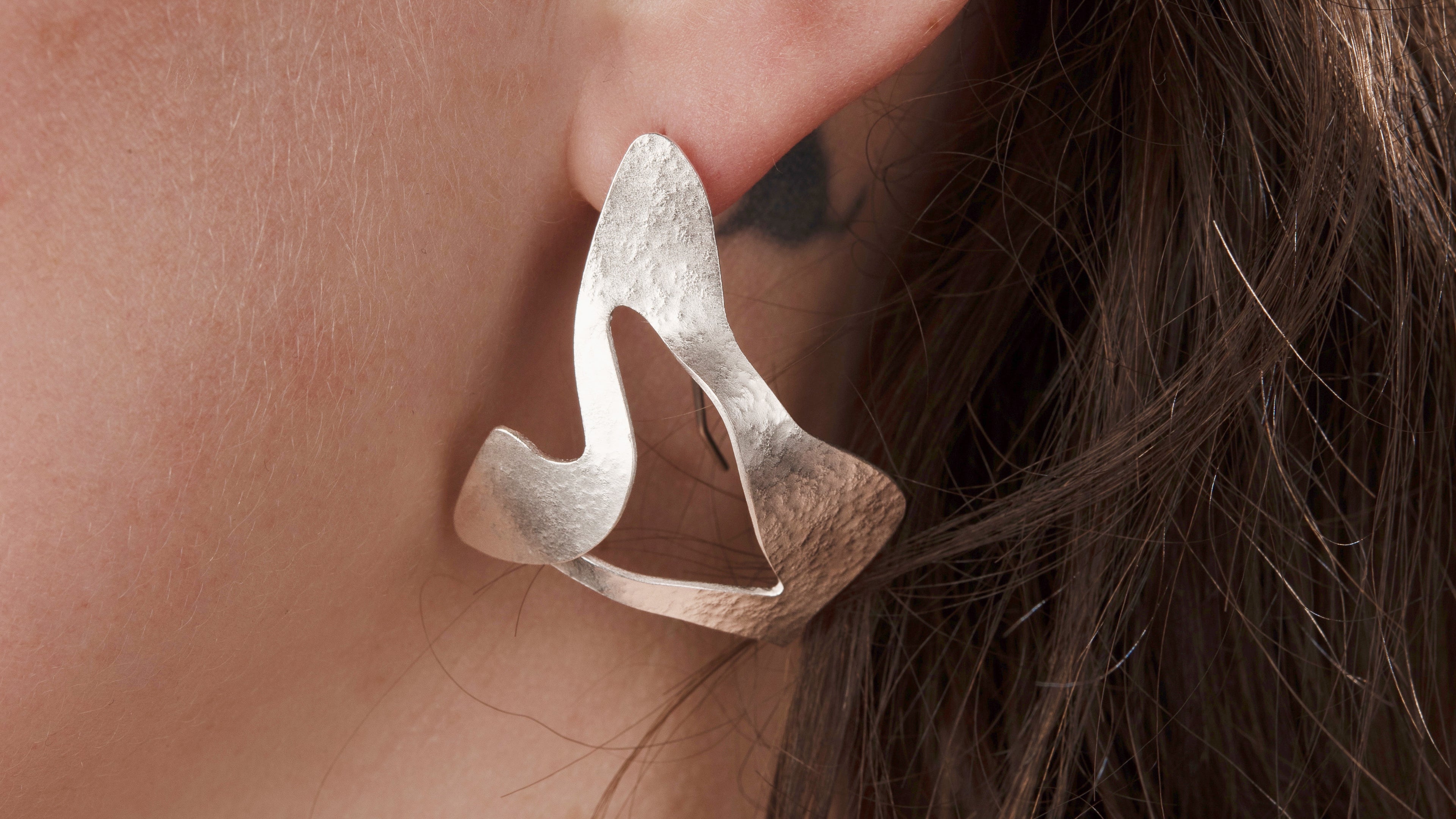 Large silver earring in abstract shape.  It has an irregular surface texture and is being worn by a women.