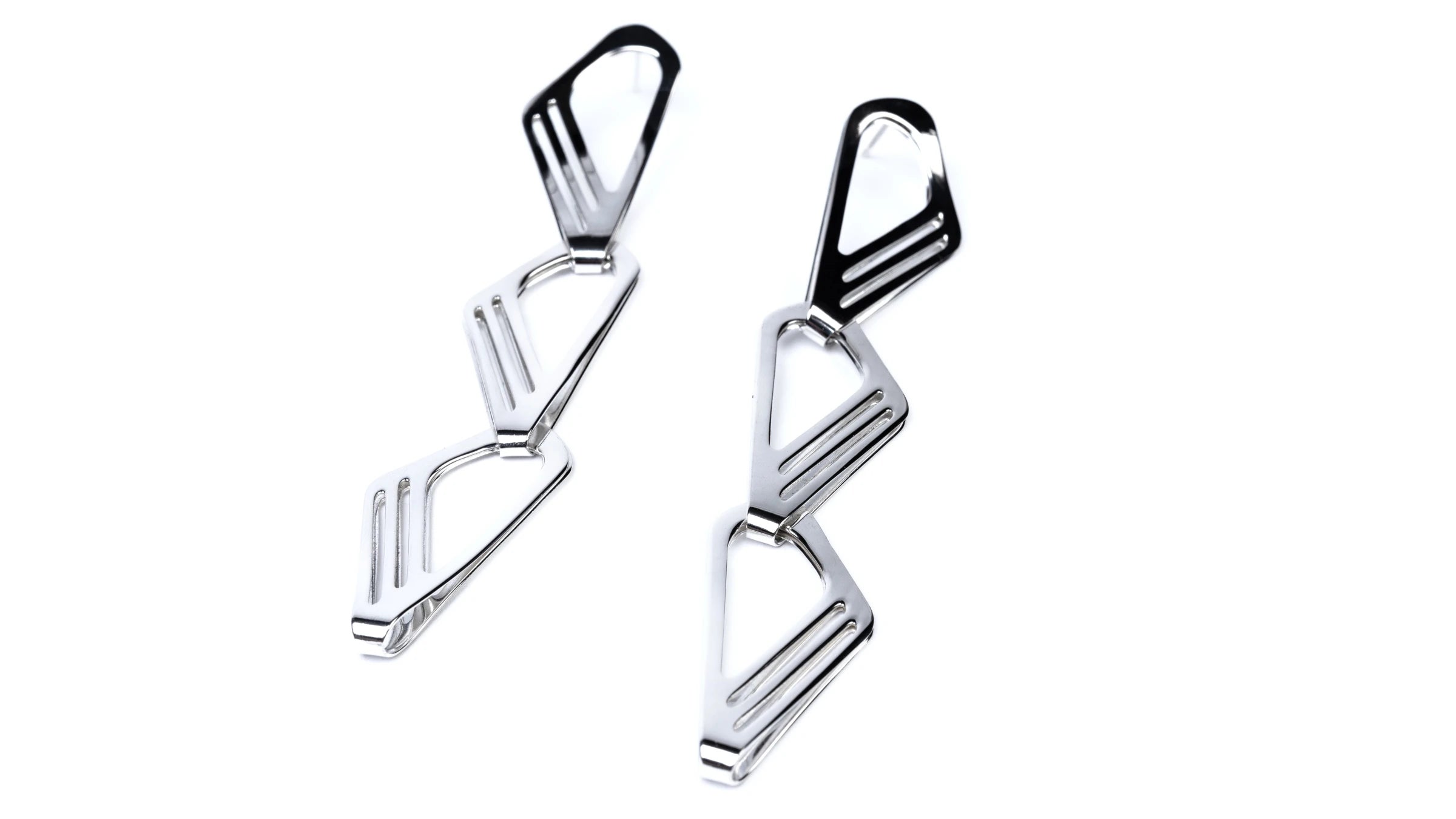A pair of llong drop shiny silver earrings made up of three repeated curved triangular shapes on a white background.
