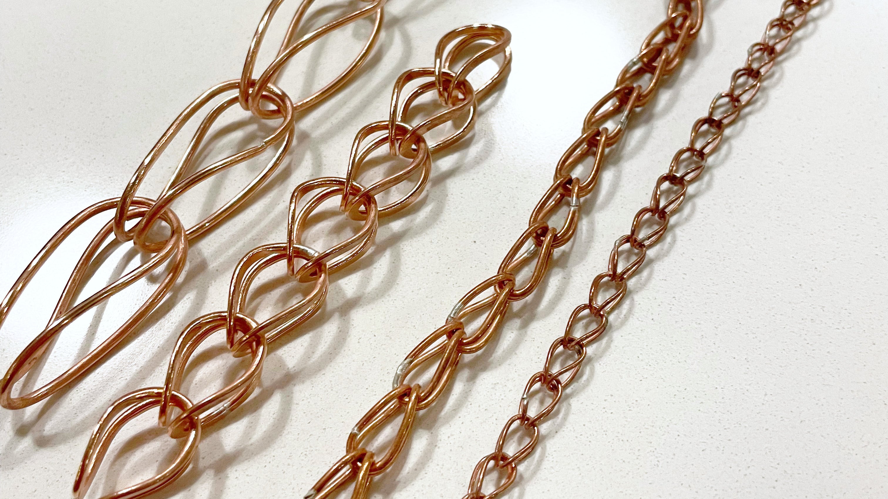 Four loop-in-loop chains made in copper wire in various sizes from small to large.