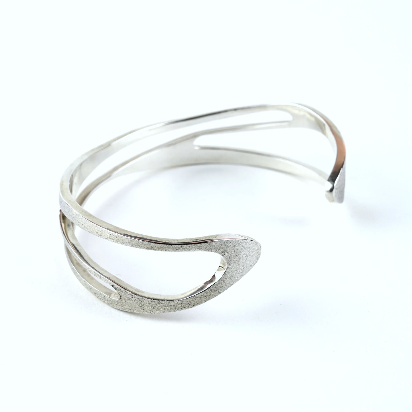 Mens silver cuff bracelet with curved shape and curved cut out areas on a white background
