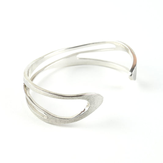 Silver cuff bracelet with curved shape and curved cut out areas on a white background