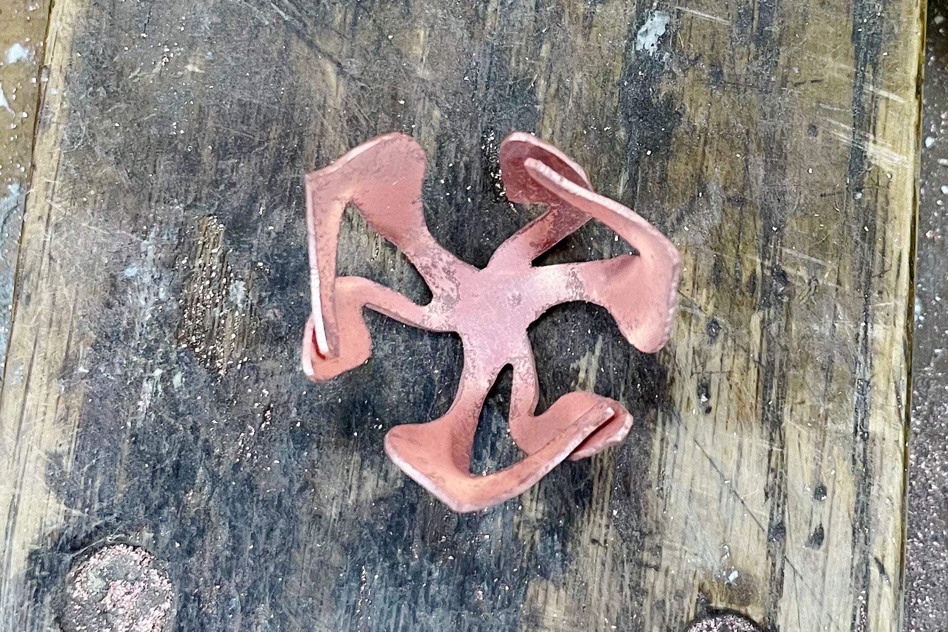 A copper test sample of an abstract flower form sitting on a jewellery workbench.