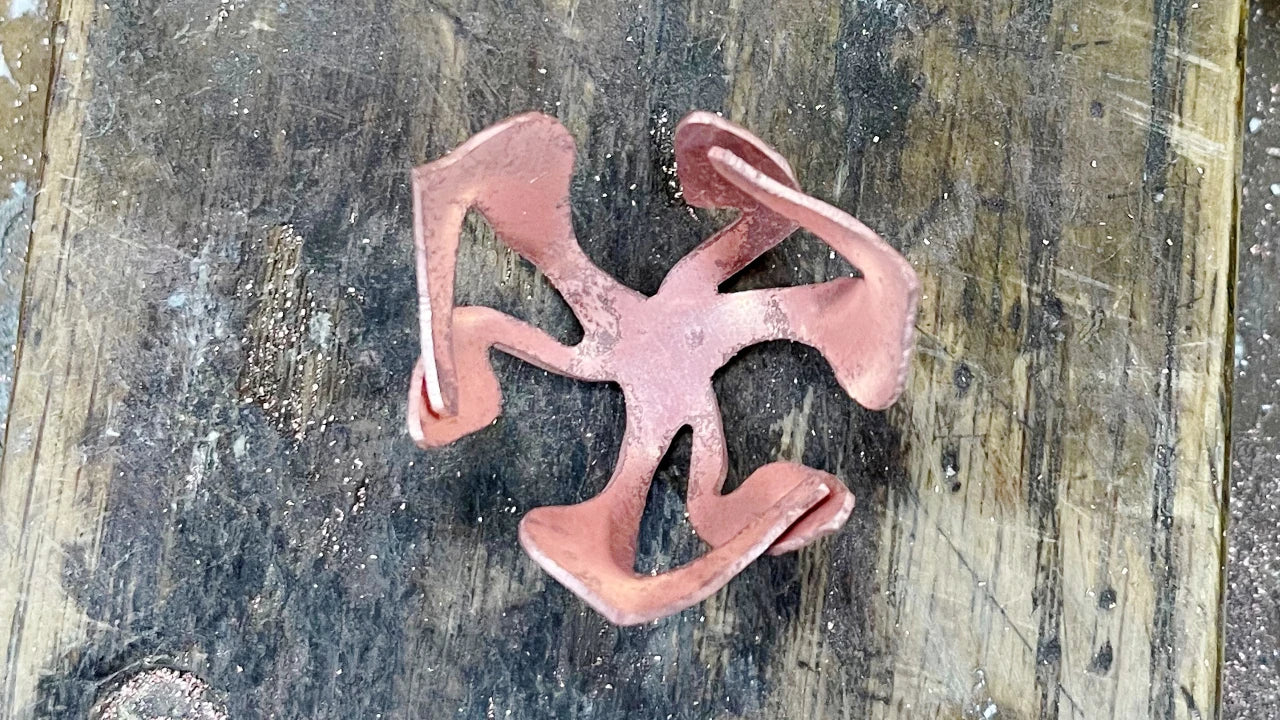 Copper shape formed into a an abstract floral shape against a wooden jewellers workbench