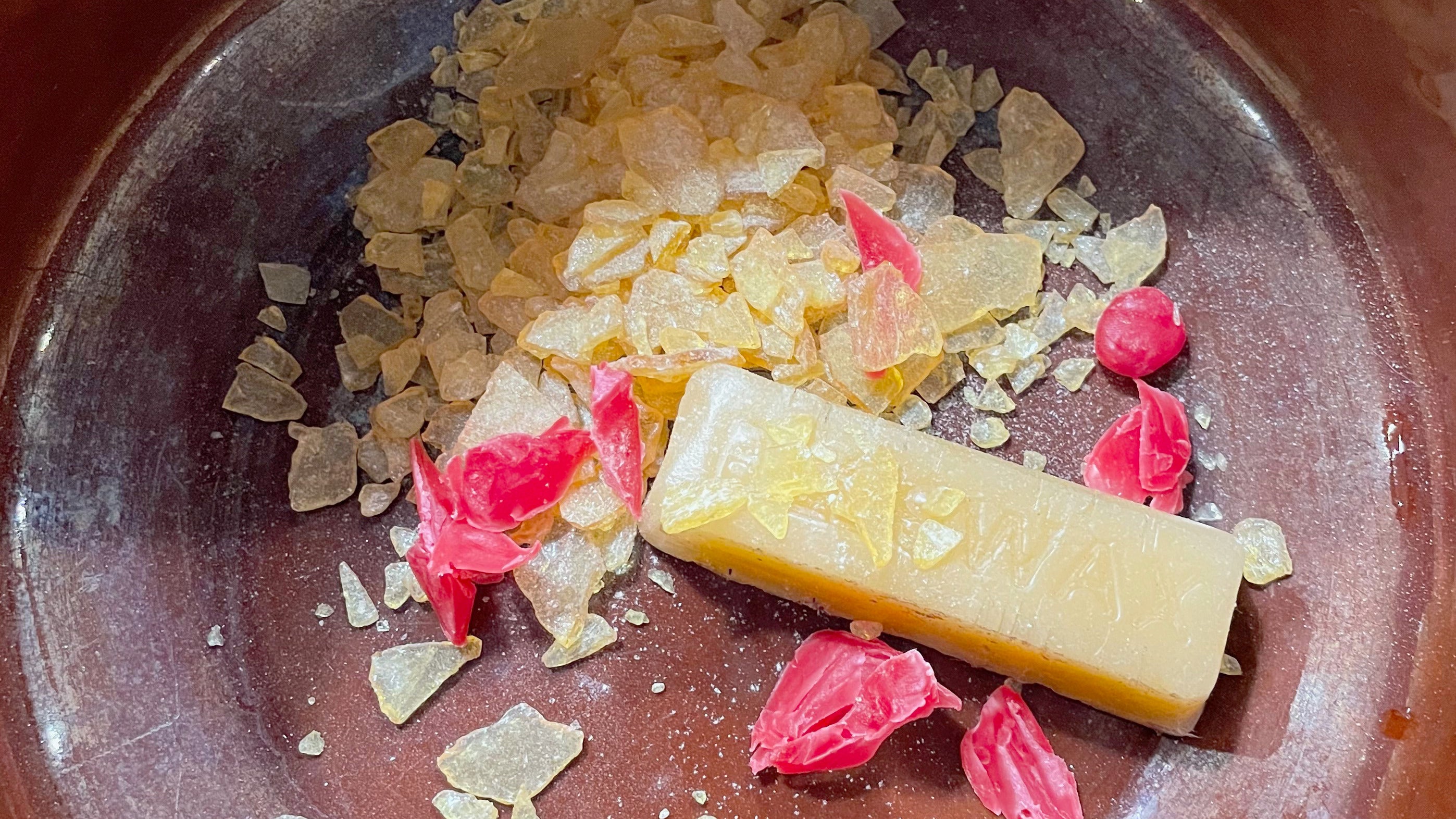 Beeswax and pieces of tree resin in a brown bowl.
