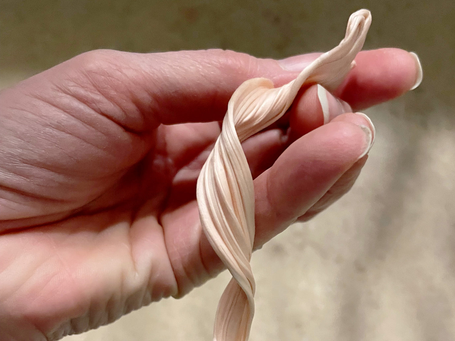 A textured strip of Mitsuro Hikime wax twisted around showing striations running along the length of the twist.  This is being held in a hand.