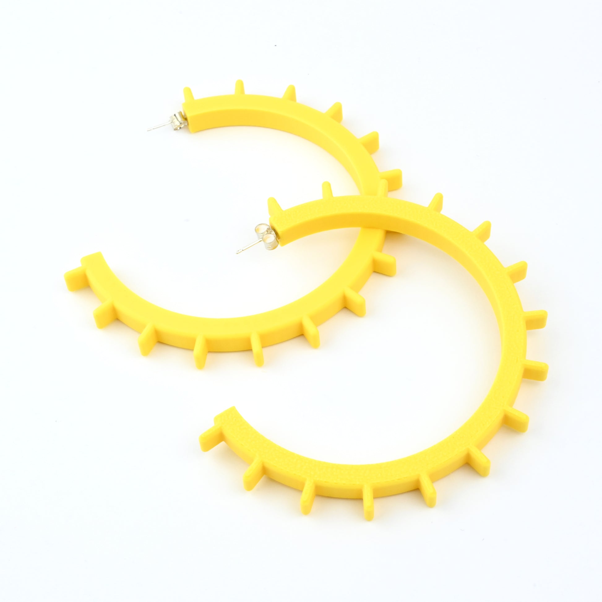 Pair of big yellow cog shaped hoop earrings with silver ear posts on a white background