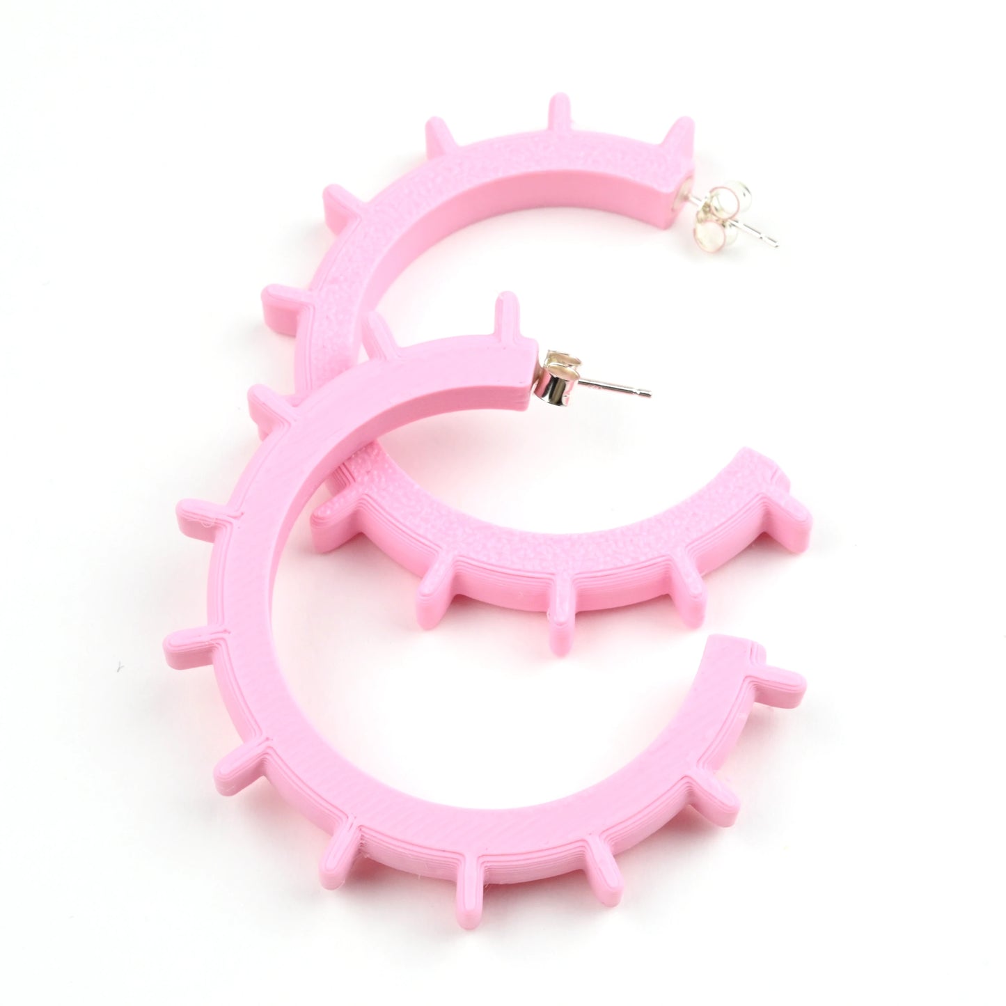 Medium pale pink hoop earrings with silver ear posts and geometric design on a white background.