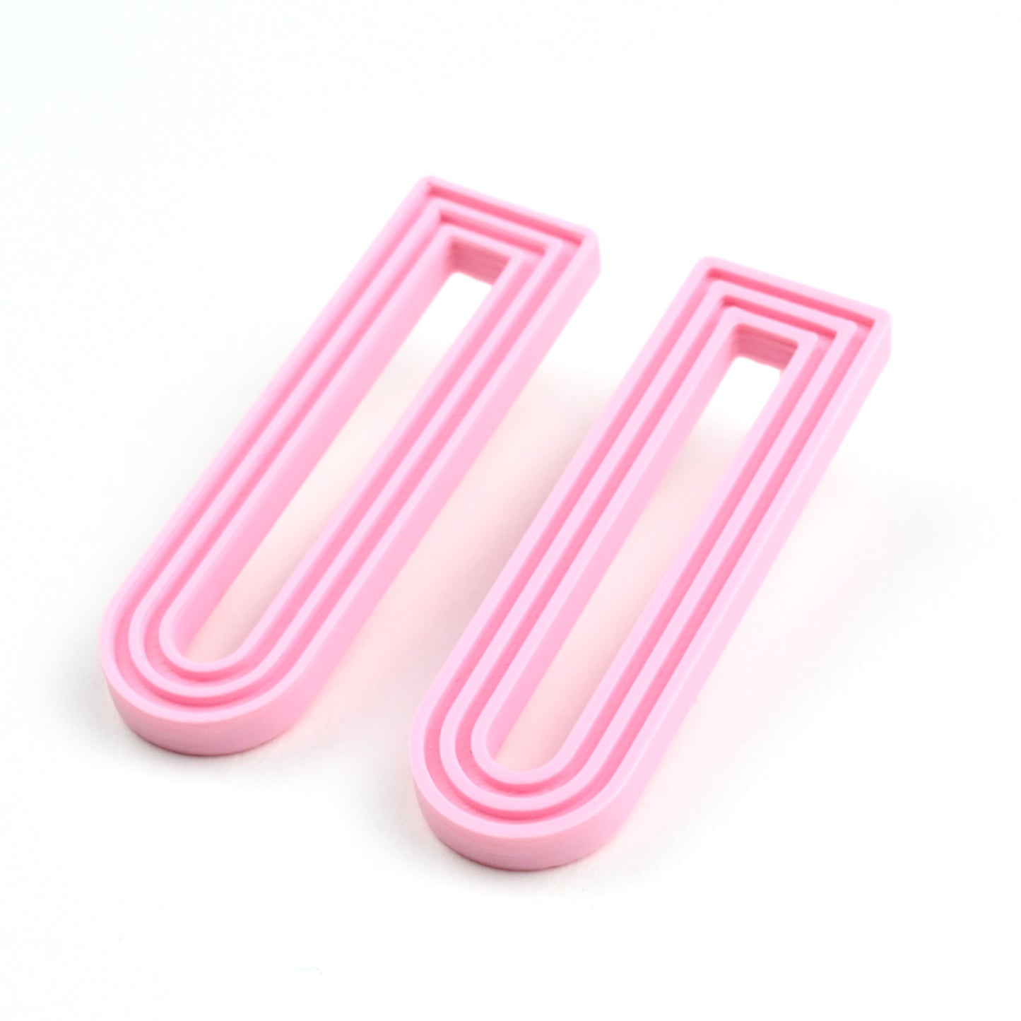 Pale pink U shaped drop earrings with raised linear design on a white background