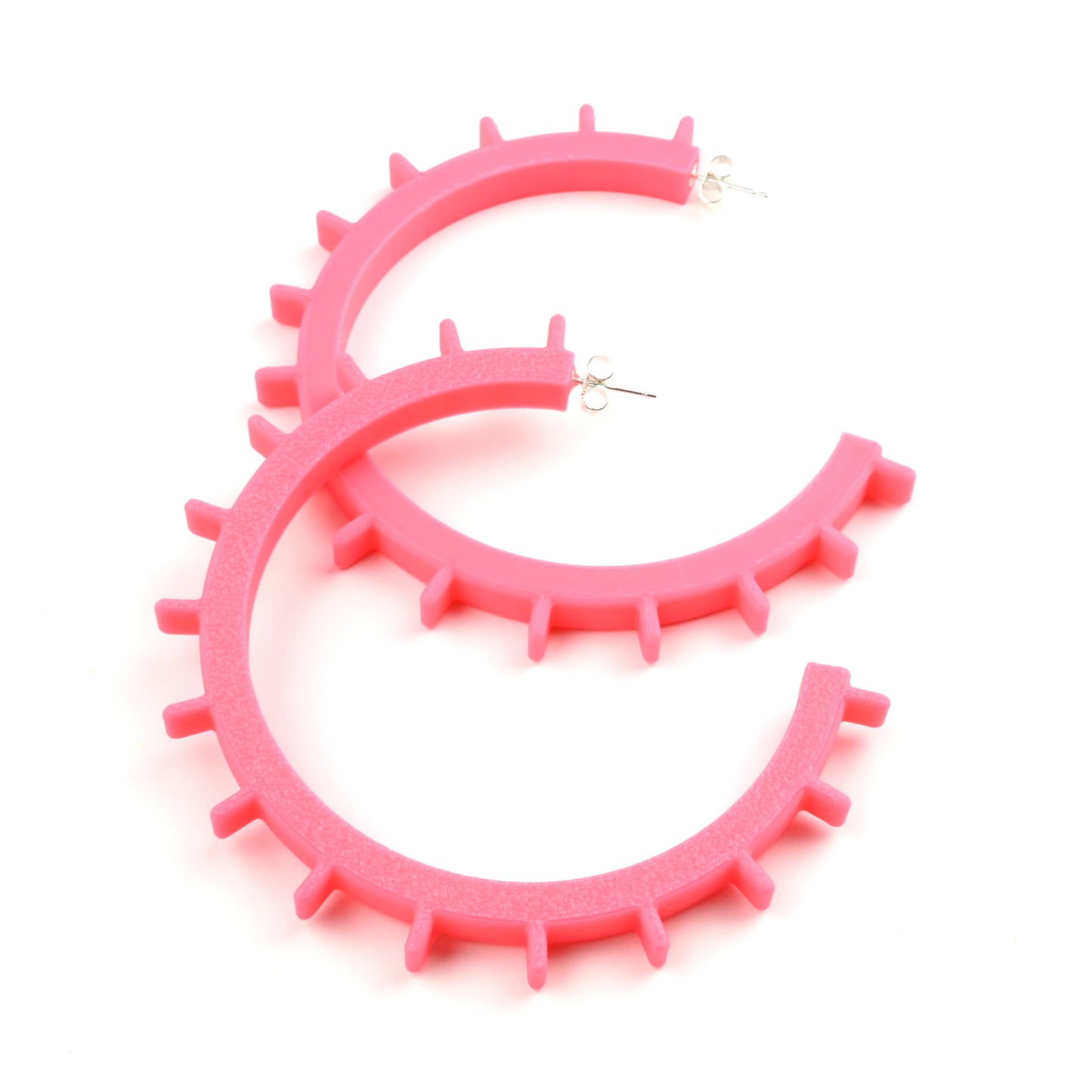Bright pink plastic hoop earrings with silver ear posts and silver earring scroll backs. The earrings are very large and have ridges sticking out along the front edge of the hoops.