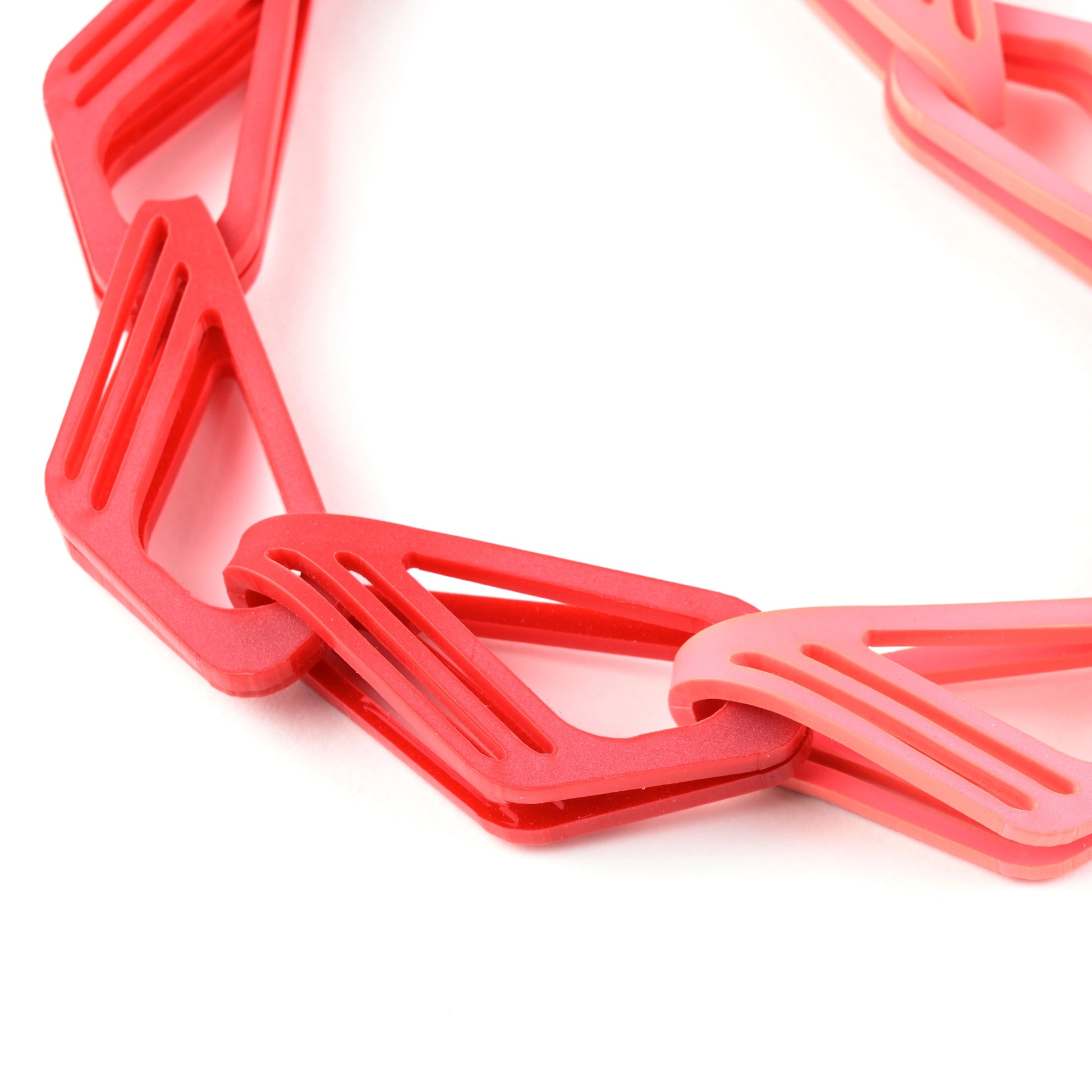 Close-up of The Halite bold, acrylic chain in red & pink with interlocking links on a white backdrop