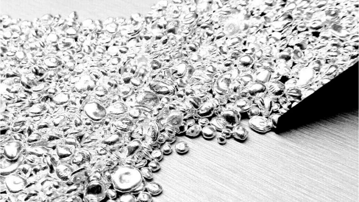 Close-up of silver casting grain spilling across a white surface