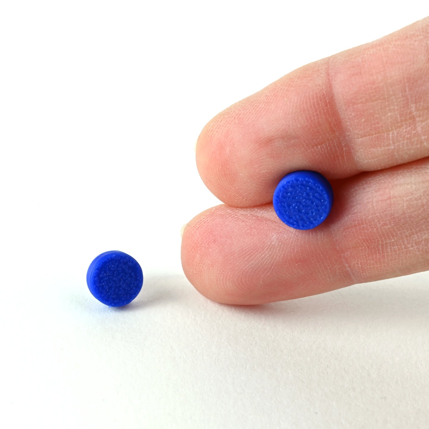 Blue round stud earrings held between two fingers on a white background