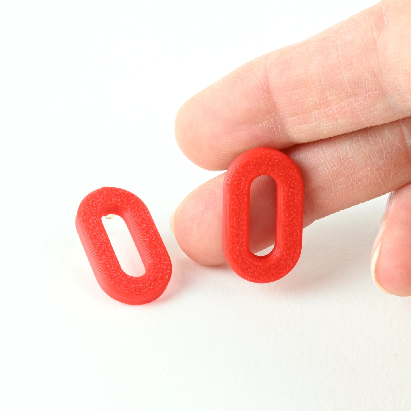 Red oval earrings with a textured surface held between fingers on a white background