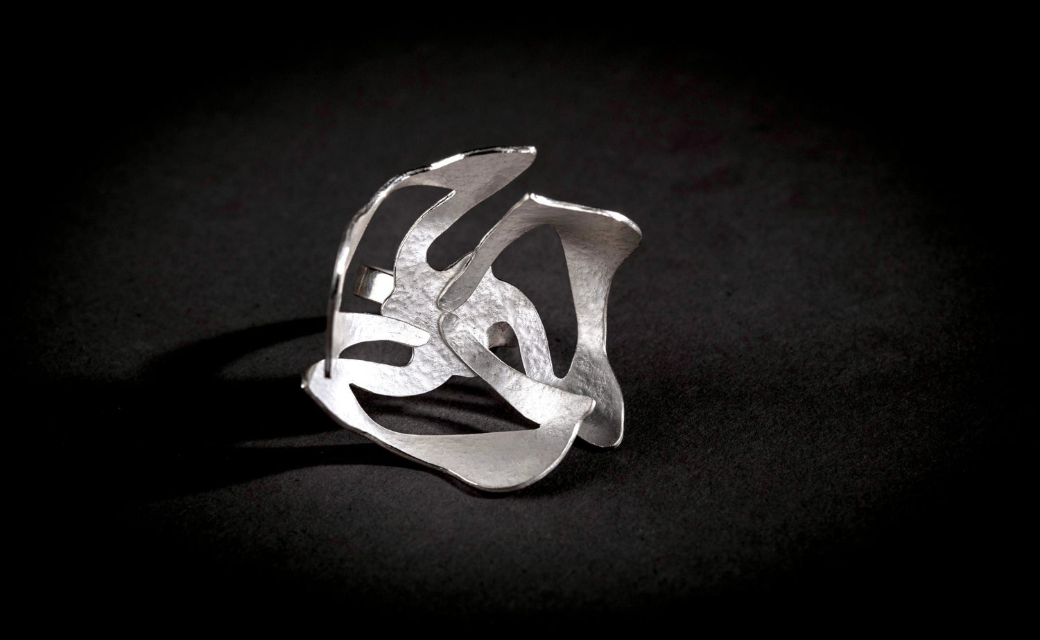 Big textured silver ring with organic shape reminiscent of a flower, on a black background 