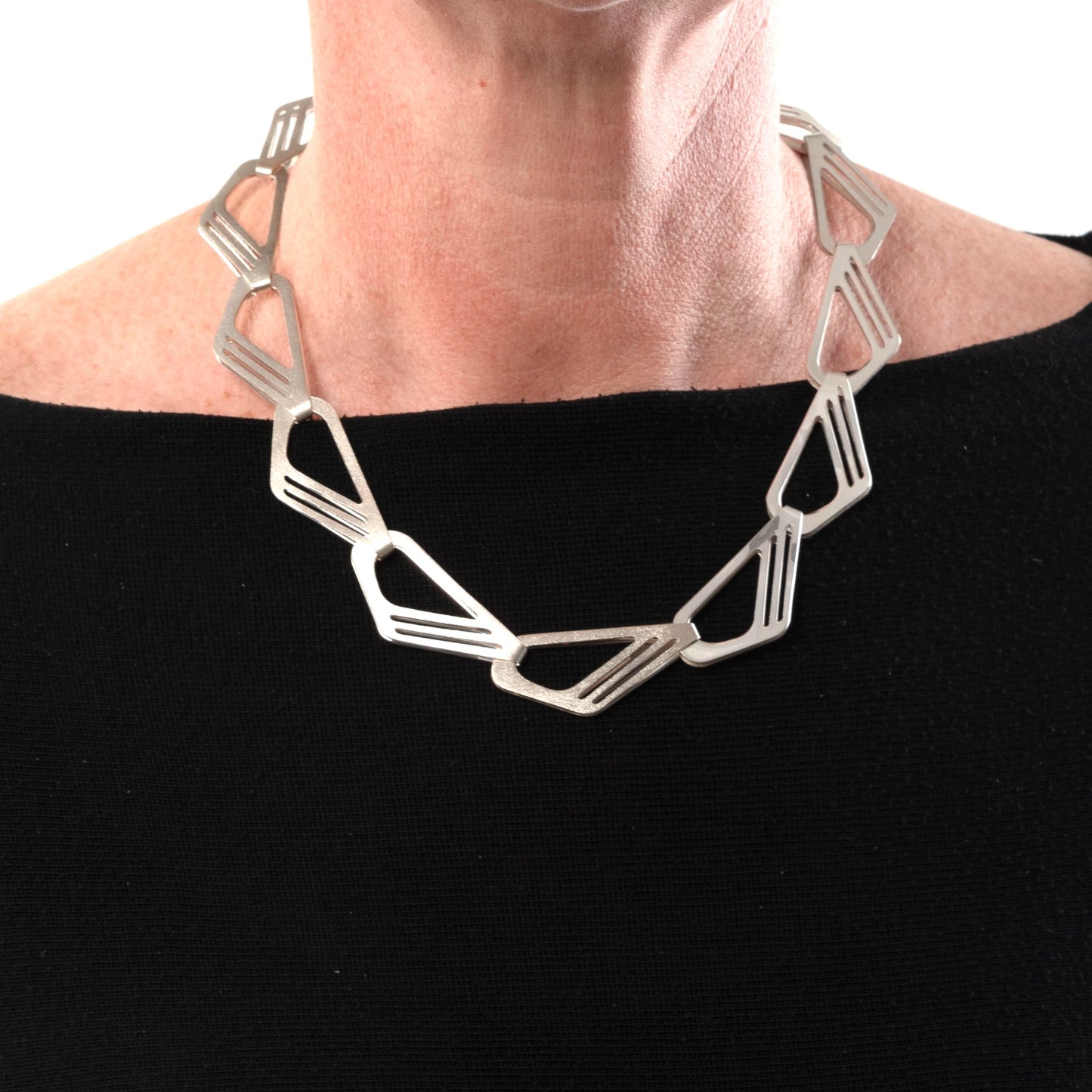 Silver geometric necklace worn by a person on a black background