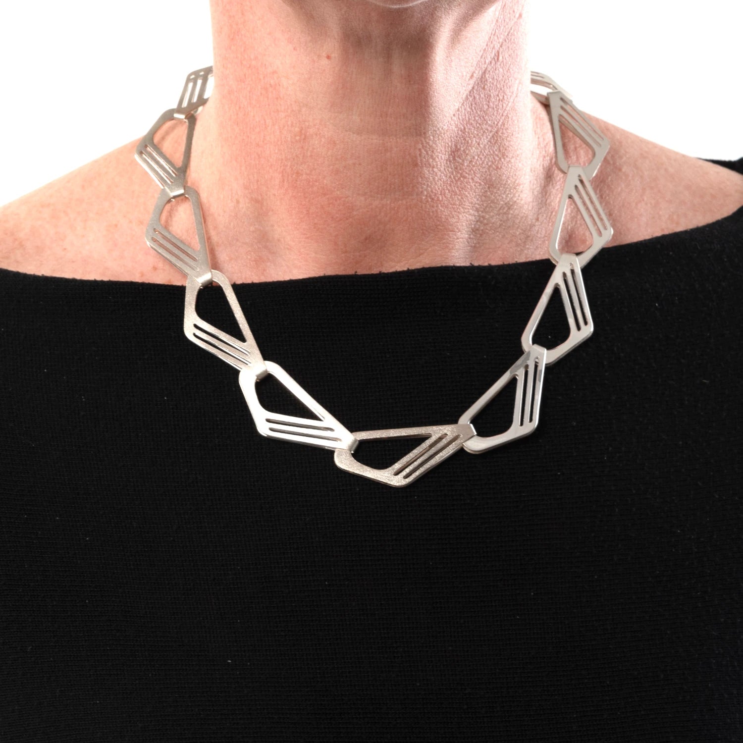 Silver geometric necklace worn by a person on a black background