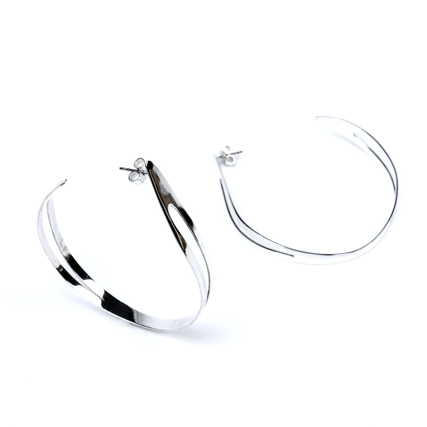 pair of large silver hoop earrings with cut out sections, one upright and one lying on its side against a white background