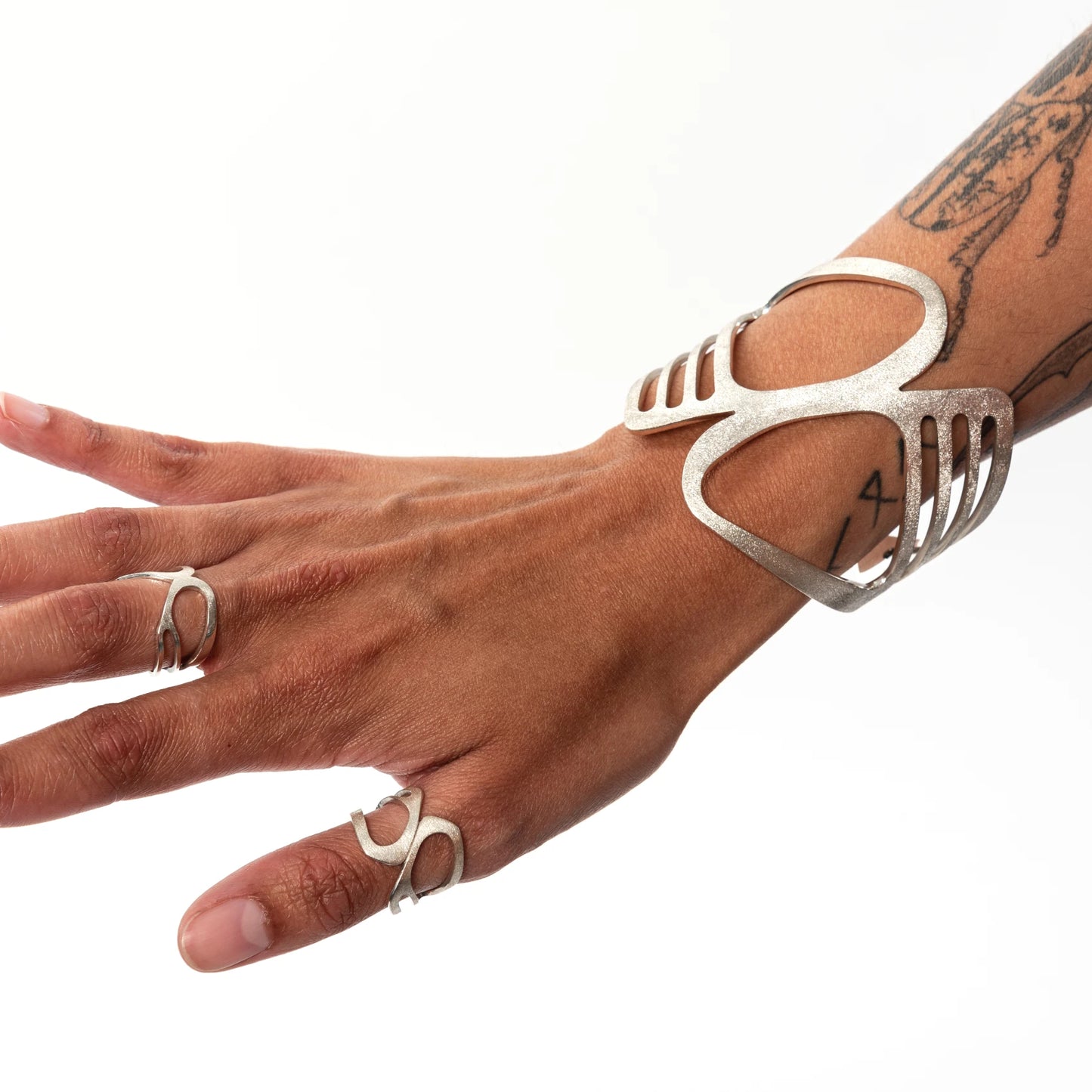 Hand wearing a wide silver cuff with cut out details and matching rings on a white background