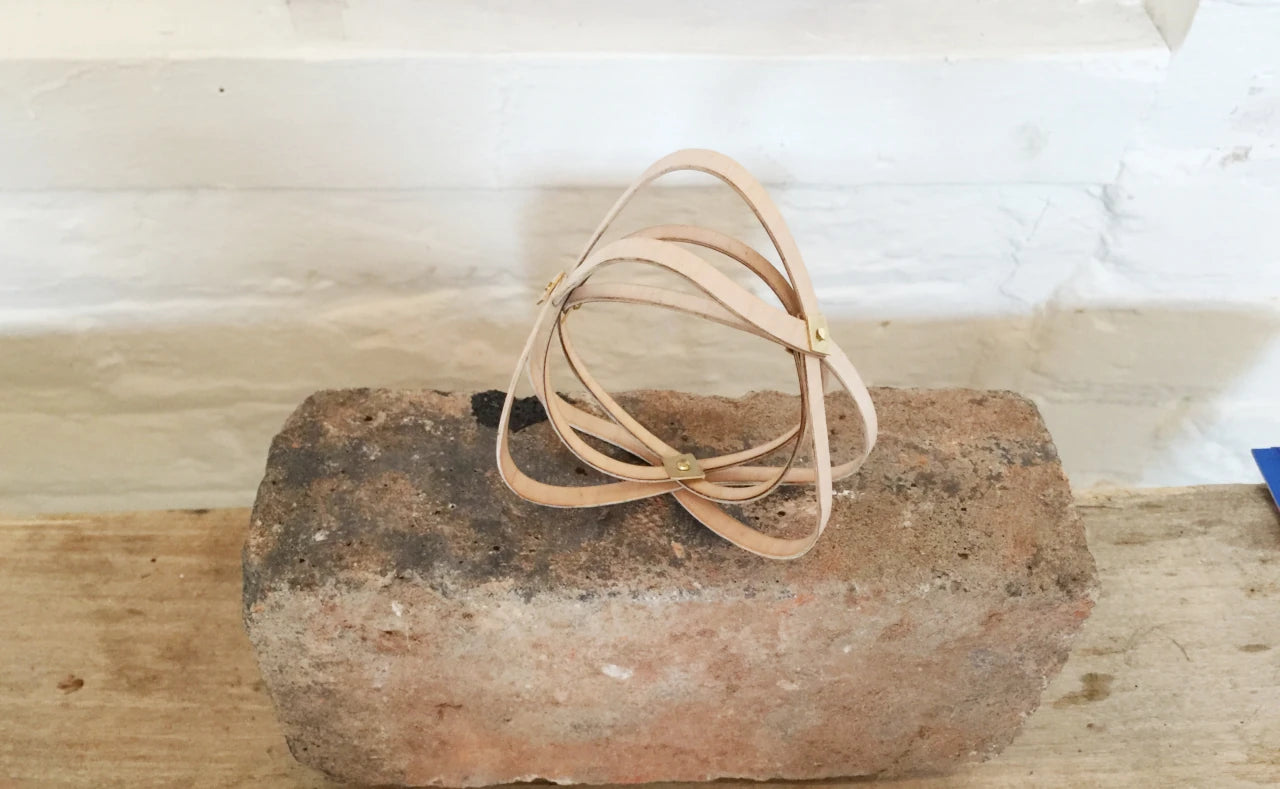 Unusual organic shaped wooden bangle made of thee repeating forms, sitting on a brick against a whte painted brick wall