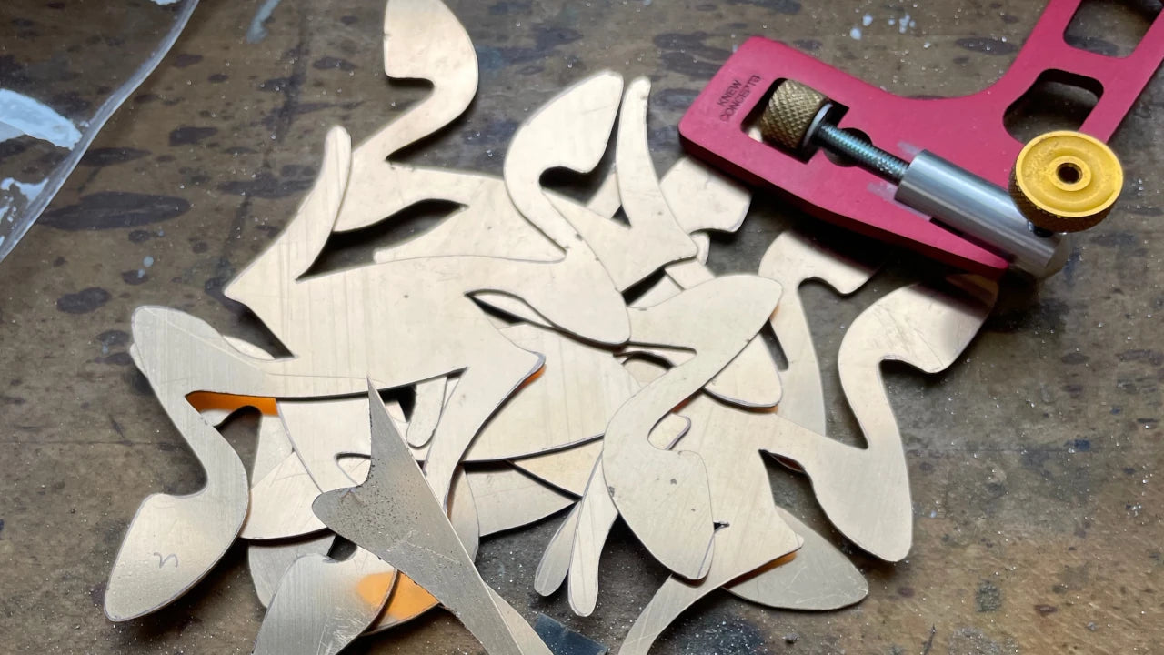 Silver cutouts waiting to be assembled on a workbench with a red piercing saw in the background